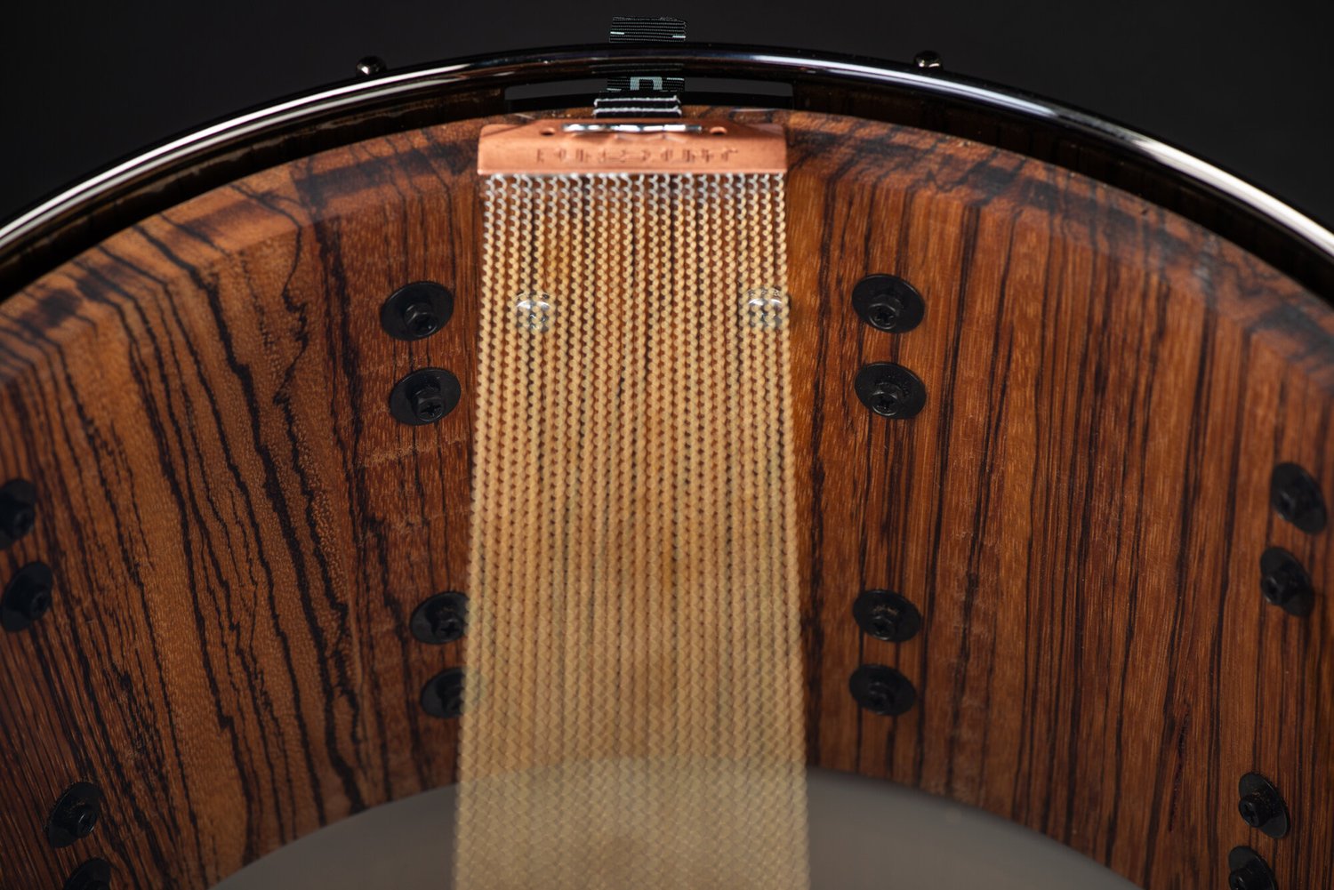 Copper snare wires stretch over a clear head, showing a natural striped hardwood interior with black lug screws.