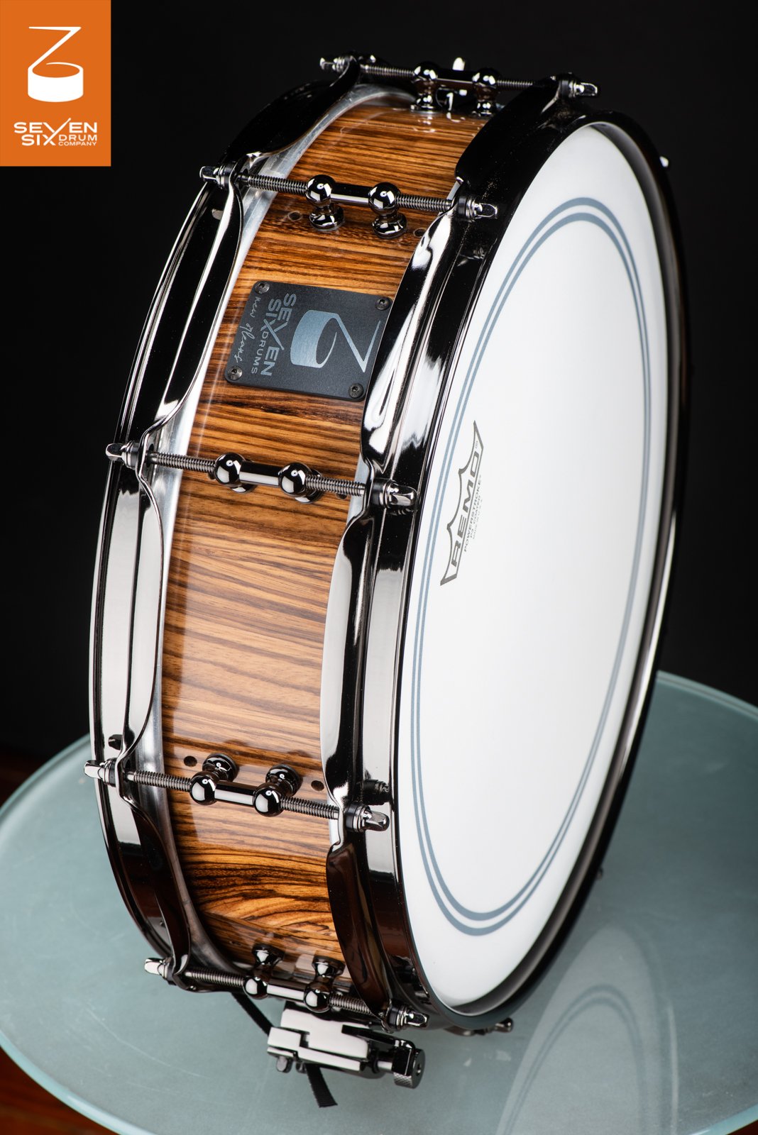 Handmade snare drum featuring a glossy striped wood shell, polished chrome hoops, and tube lugs.