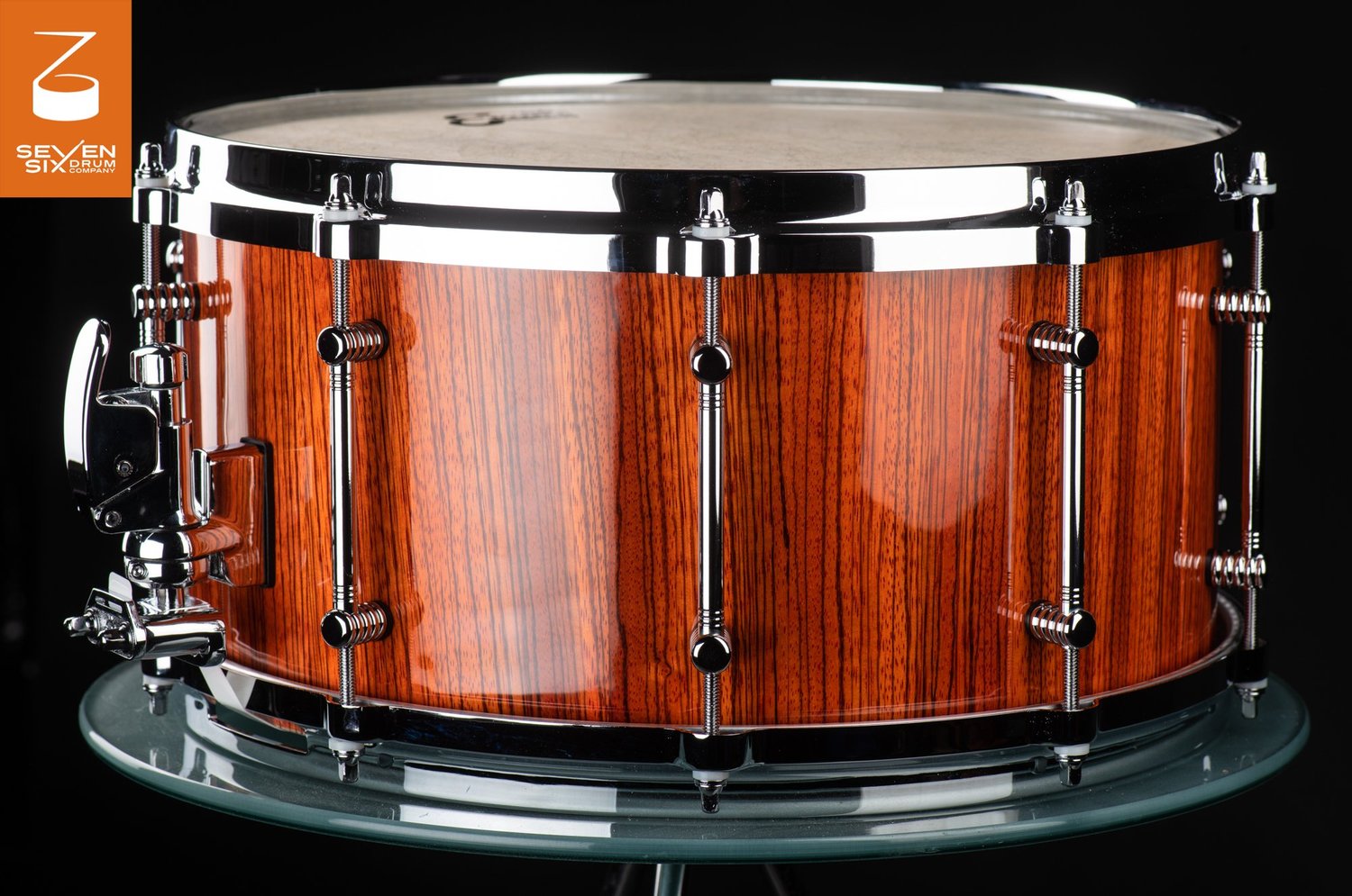 Handmade snare drum with a high-gloss striped wood shell, chrome tube lugs, and polished chrome hoops.