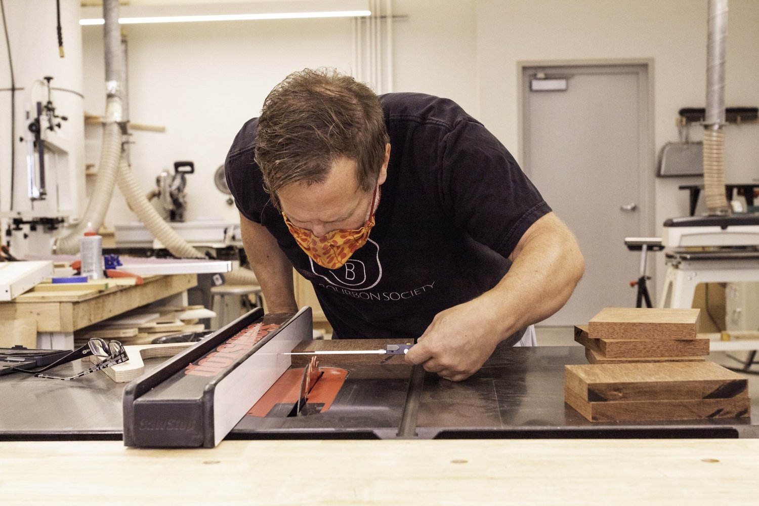 A craftsman measures unfinished hardwood drum staves using digital calipers at a table saw.