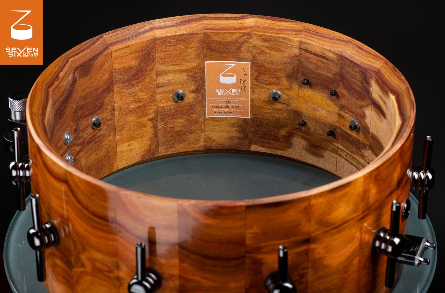 Handmade stave snare drum shell in glossy canary wood, featuring a natural wood interior and black hardware lugs.