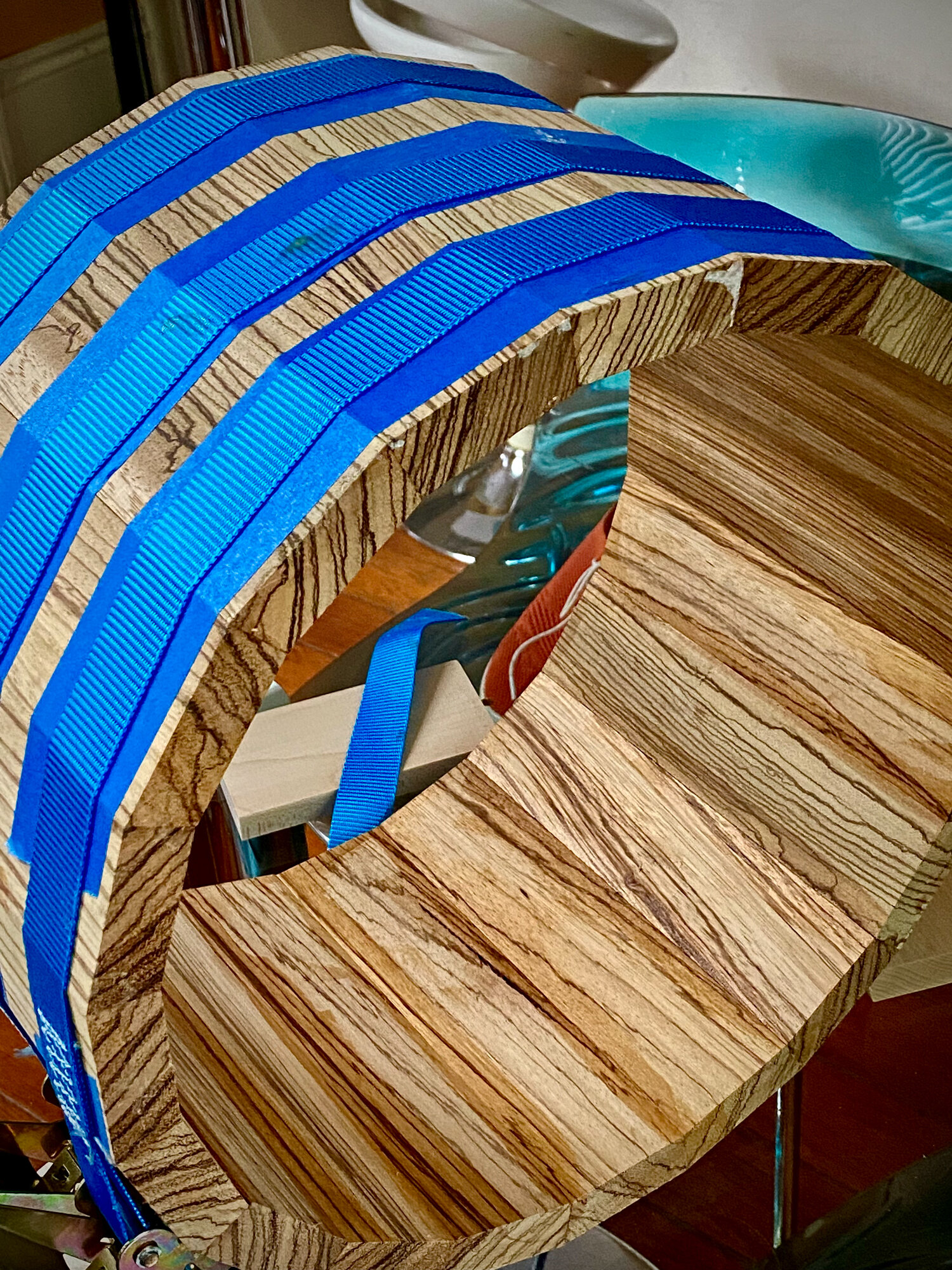 Unfinished zebrawood stave drum shell clamped together with blue ratchet straps during assembly.