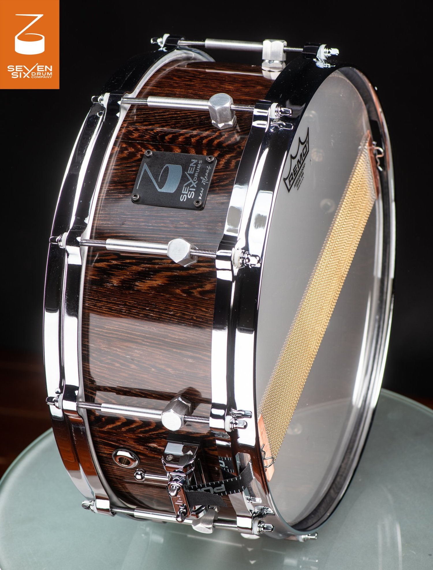 Handmade snare drum with a glossy dark wood shell, polished chrome hardware, and wide brass snare wires.
