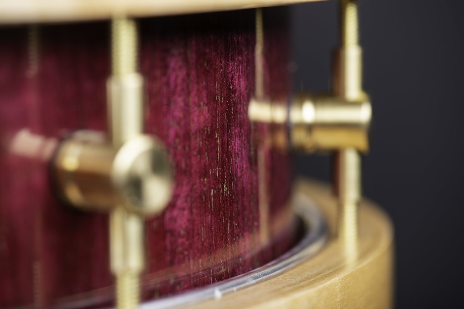 Handmade snare drum featuring a purple wood grain shell, natural wood hoops, and brass tension lugs.
