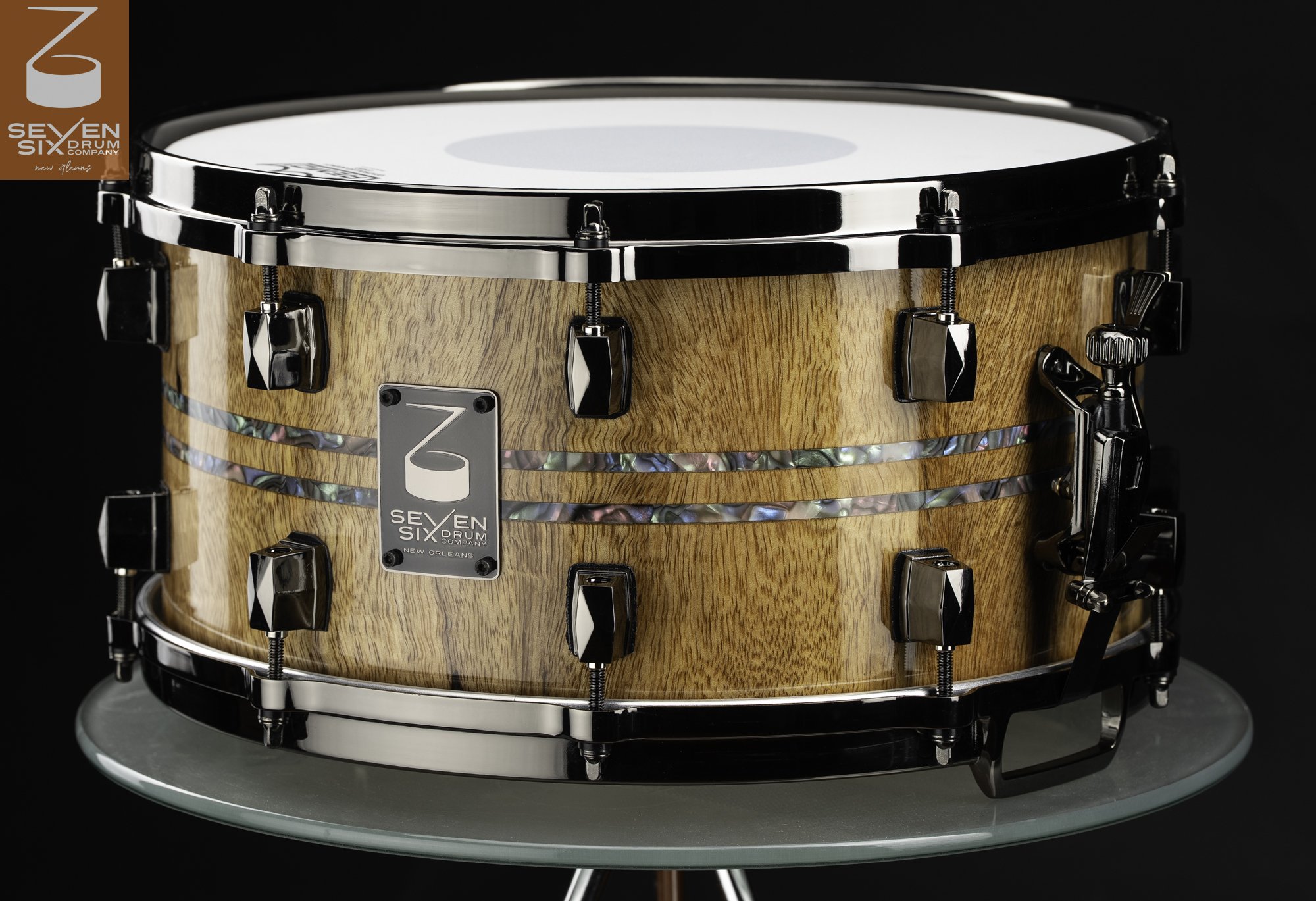 Glossy natural wood snare drum featuring dual abalone inlays and polished black nickel hardware.