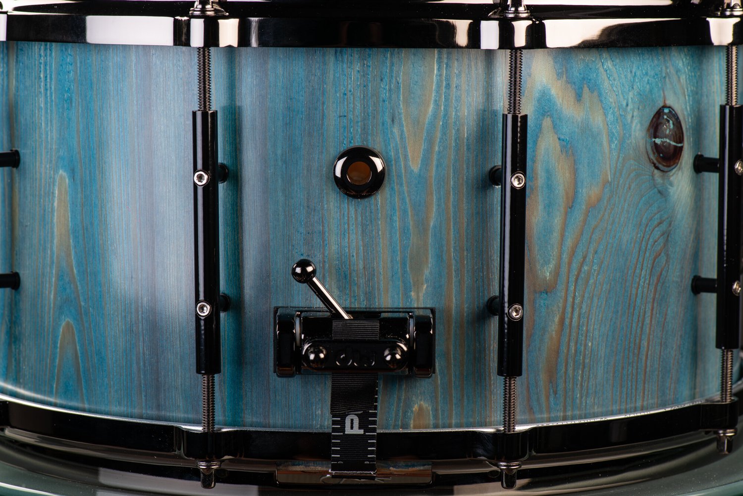 Blue-stained wood grain snare drum featuring glossy black nickel hoops, tube lugs, and a snare throw-off.