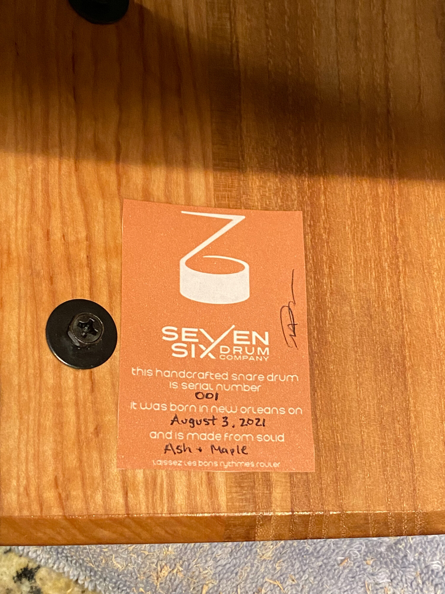 Interior maker's label on a natural-finish solid ash and maple snare drum shell beside a black mounting screw.