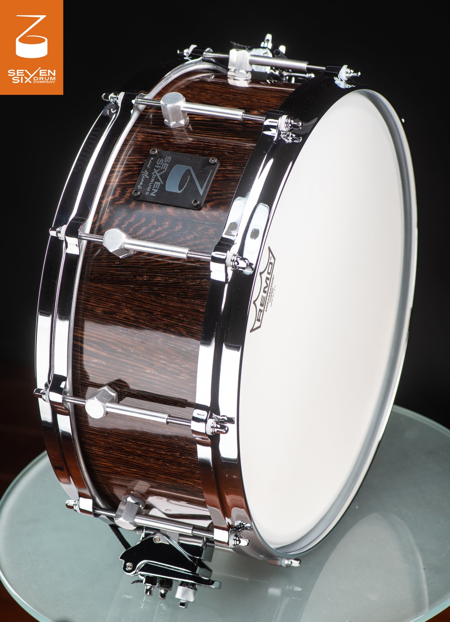 Handmade snare drum with a glossy dark wood shell, chrome hoops, and polished metal lugs.