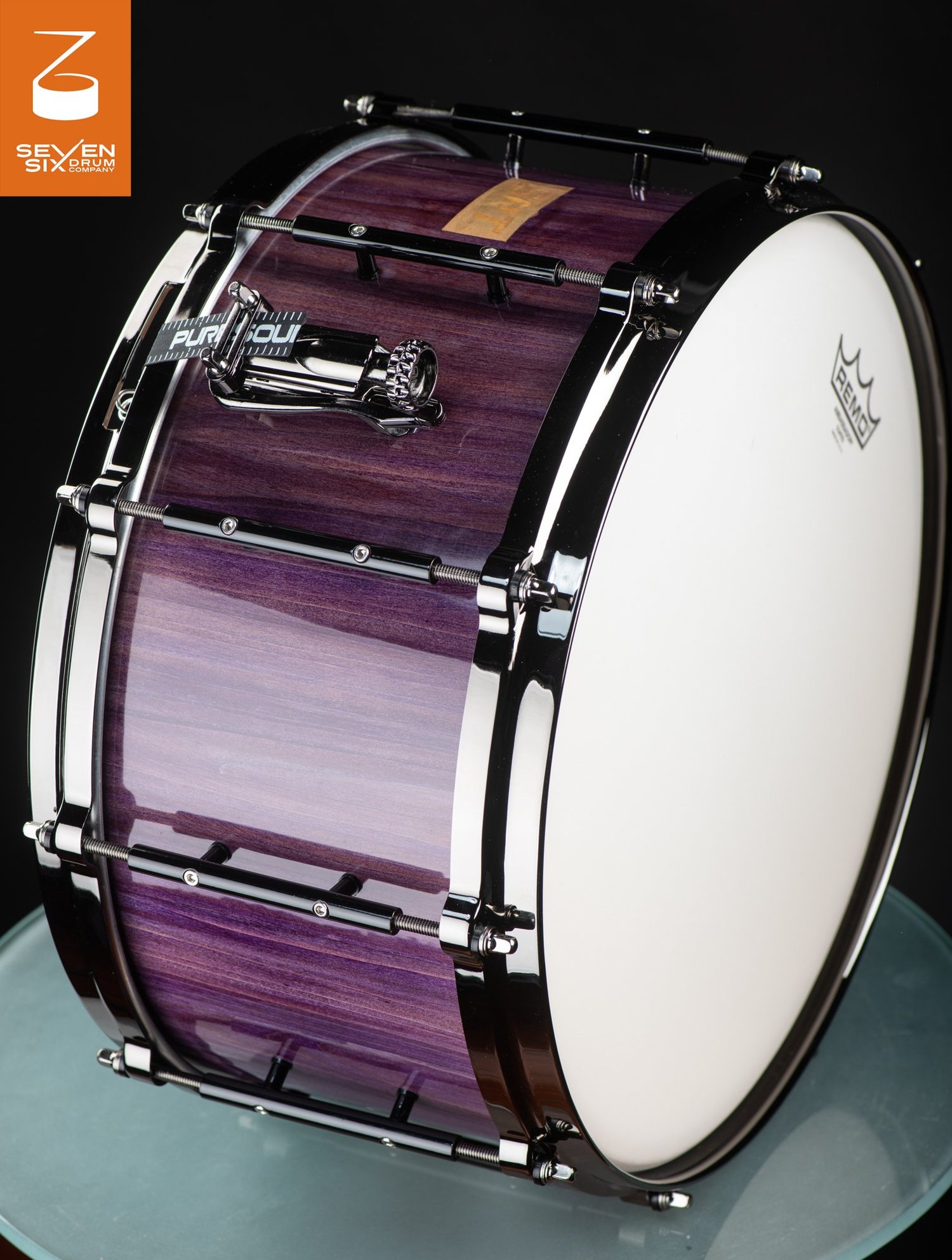 Handmade snare drum featuring a glossy purple wood shell, sleek black nickel hoops, tube lugs, and a chrome throw-off.