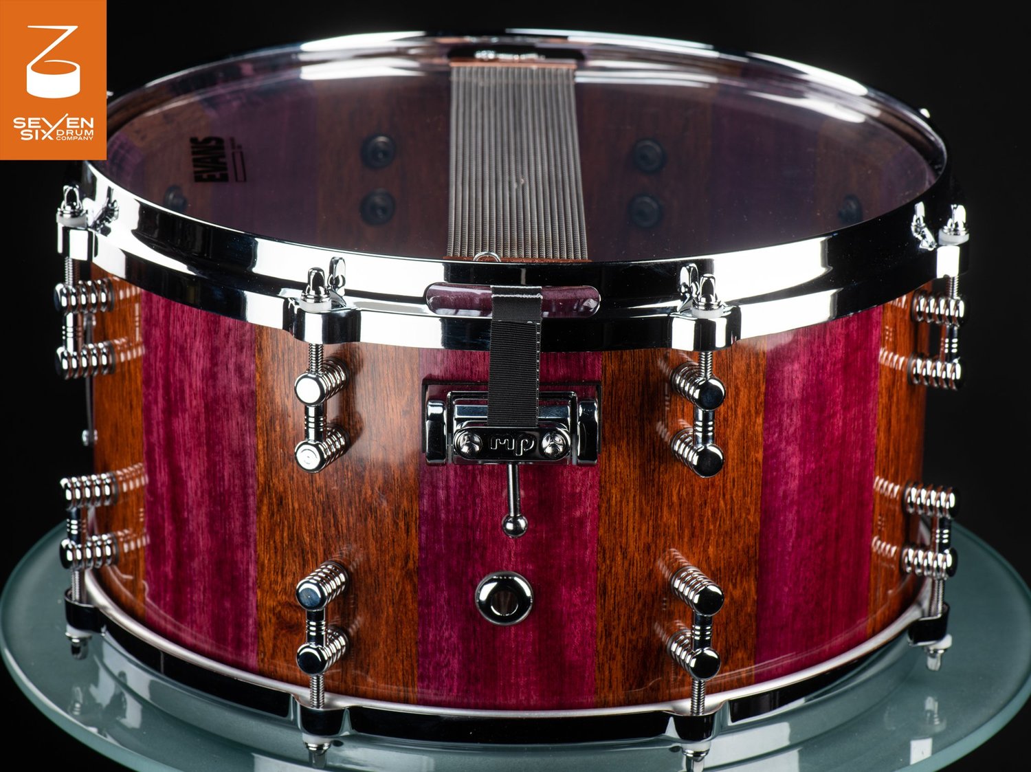Handmade snare drum featuring a glossy purpleheart and brown striped wood shell, chrome hoops, and ribbed lugs.