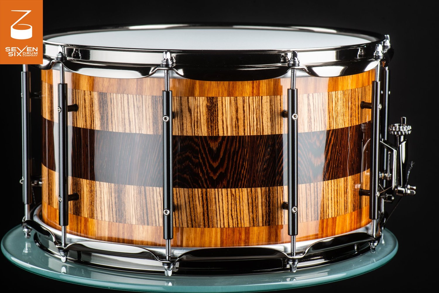 Handmade snare drum with a high-gloss striped wood shell, black tube lugs, and polished chrome hardware.