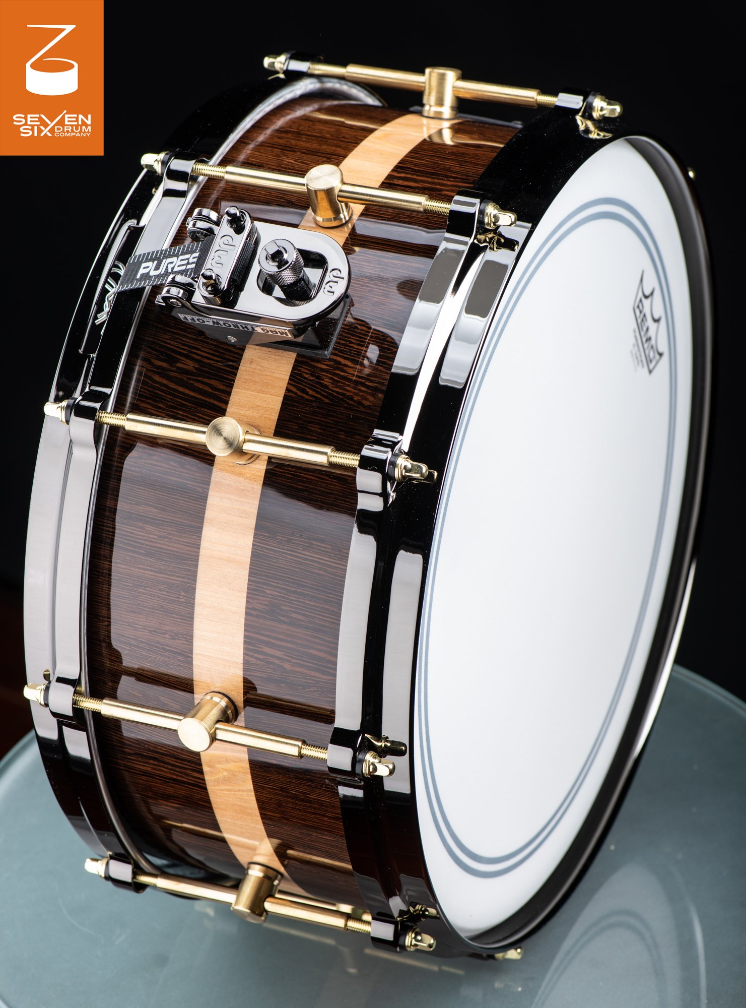 Glossy dark wood snare drum featuring a light wood center stripe, black hoops, and brass tube lugs.