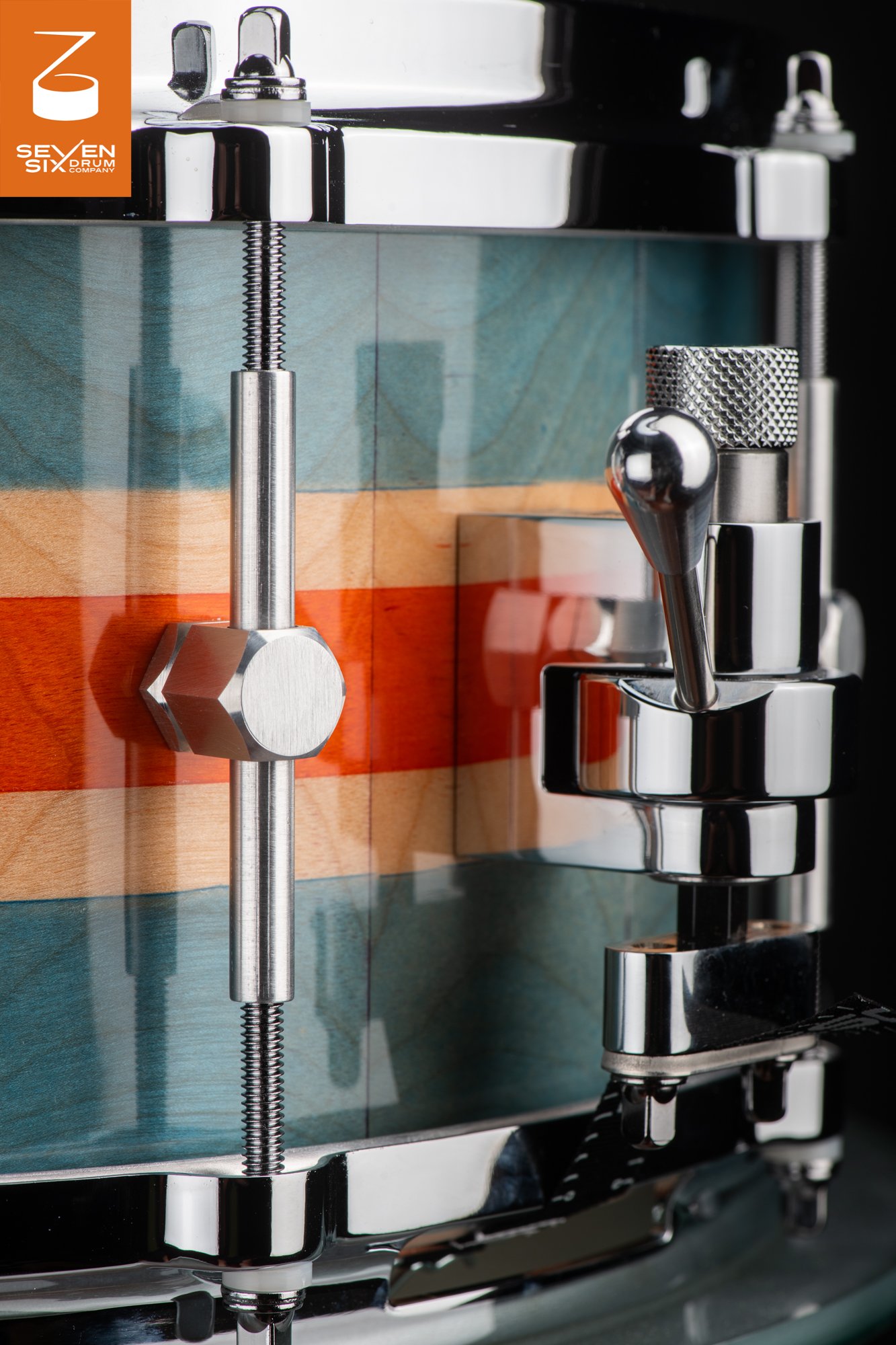 Glossy wood snare drum with teal and orange stripes, featuring a brushed hex lug and polished chrome snare throw-off.