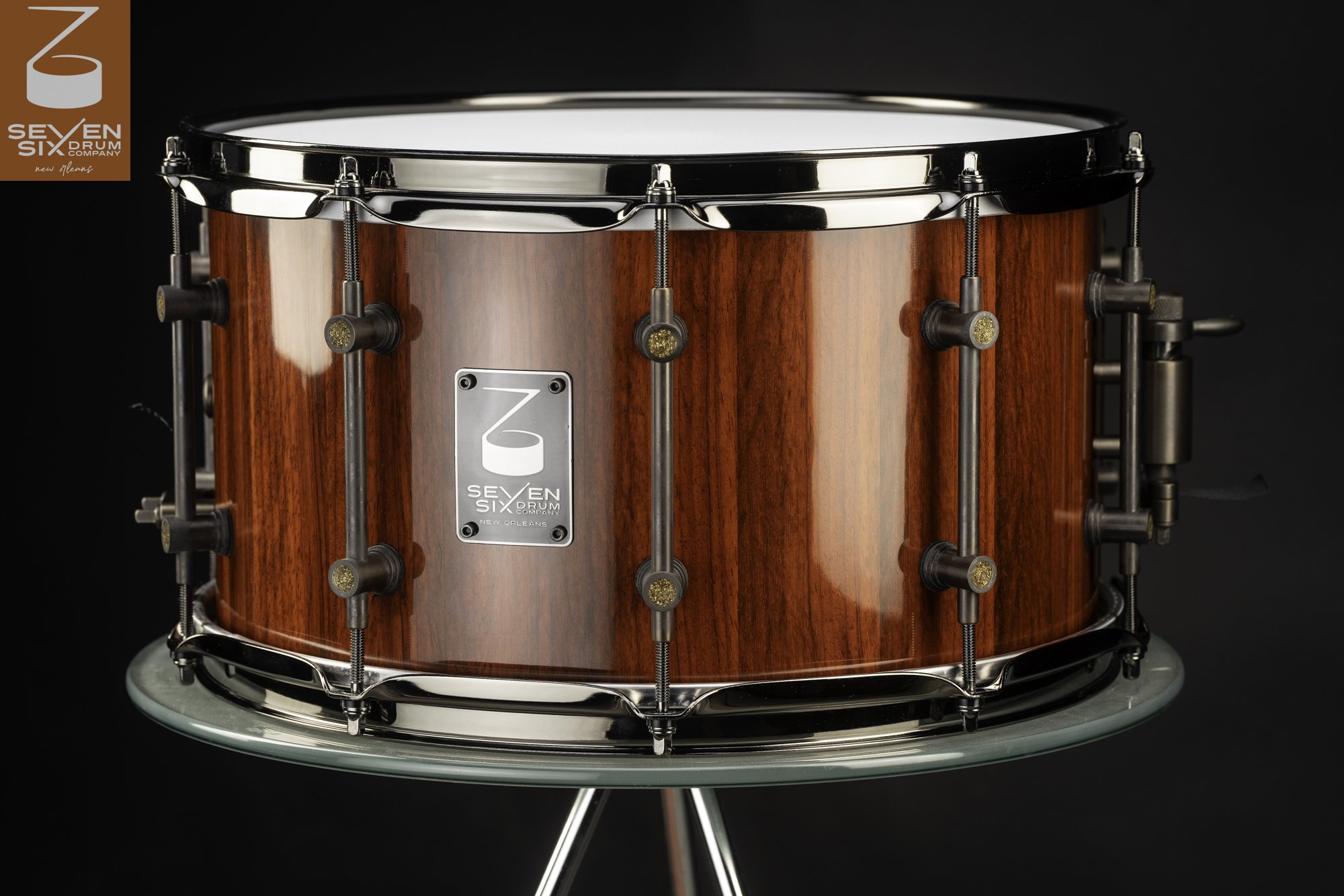 Handmade snare drum with a glossy red wood shell, antiqued bronze tube lugs, and polished dark chrome hoops.