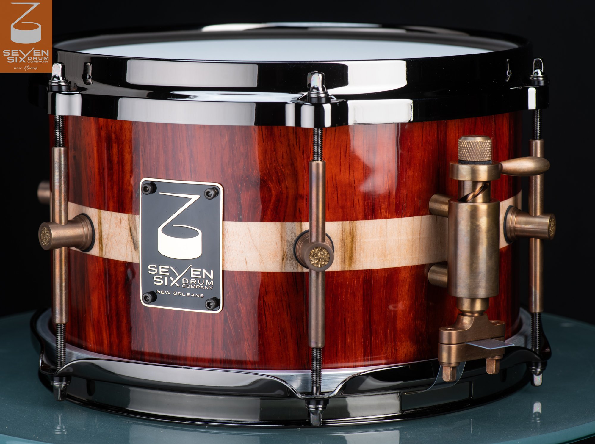 Handmade glossy red wood snare drum with a light wood stripe, antique brass hardware, and black hoops.