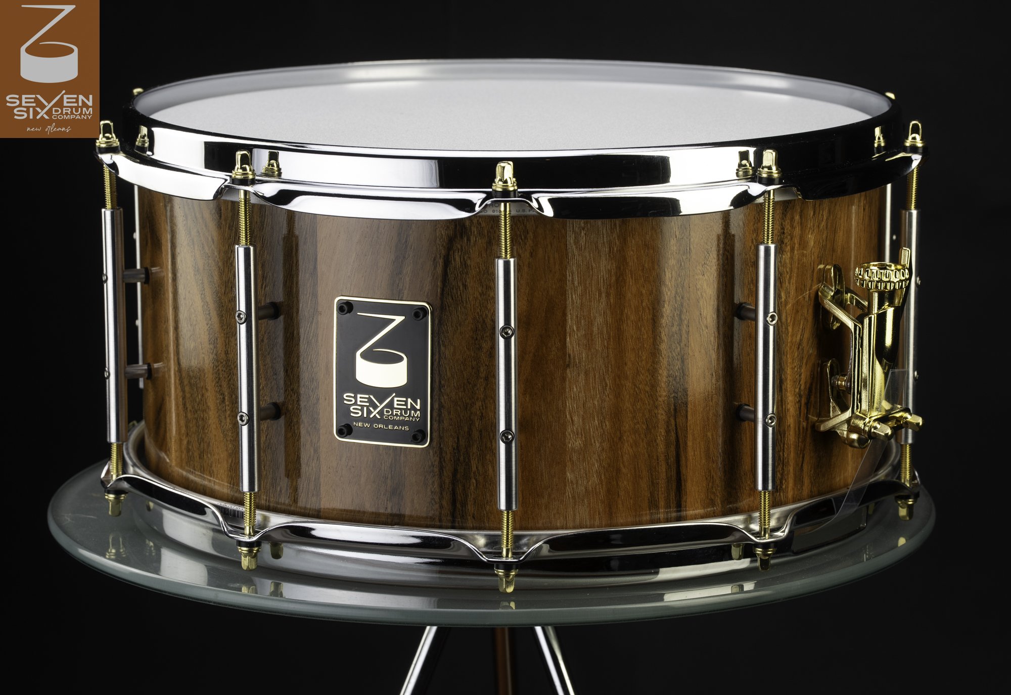 Handmade snare drum featuring a glossy wood shell, chrome hoops, silver tube lugs, and a polished gold throw-off strainer.