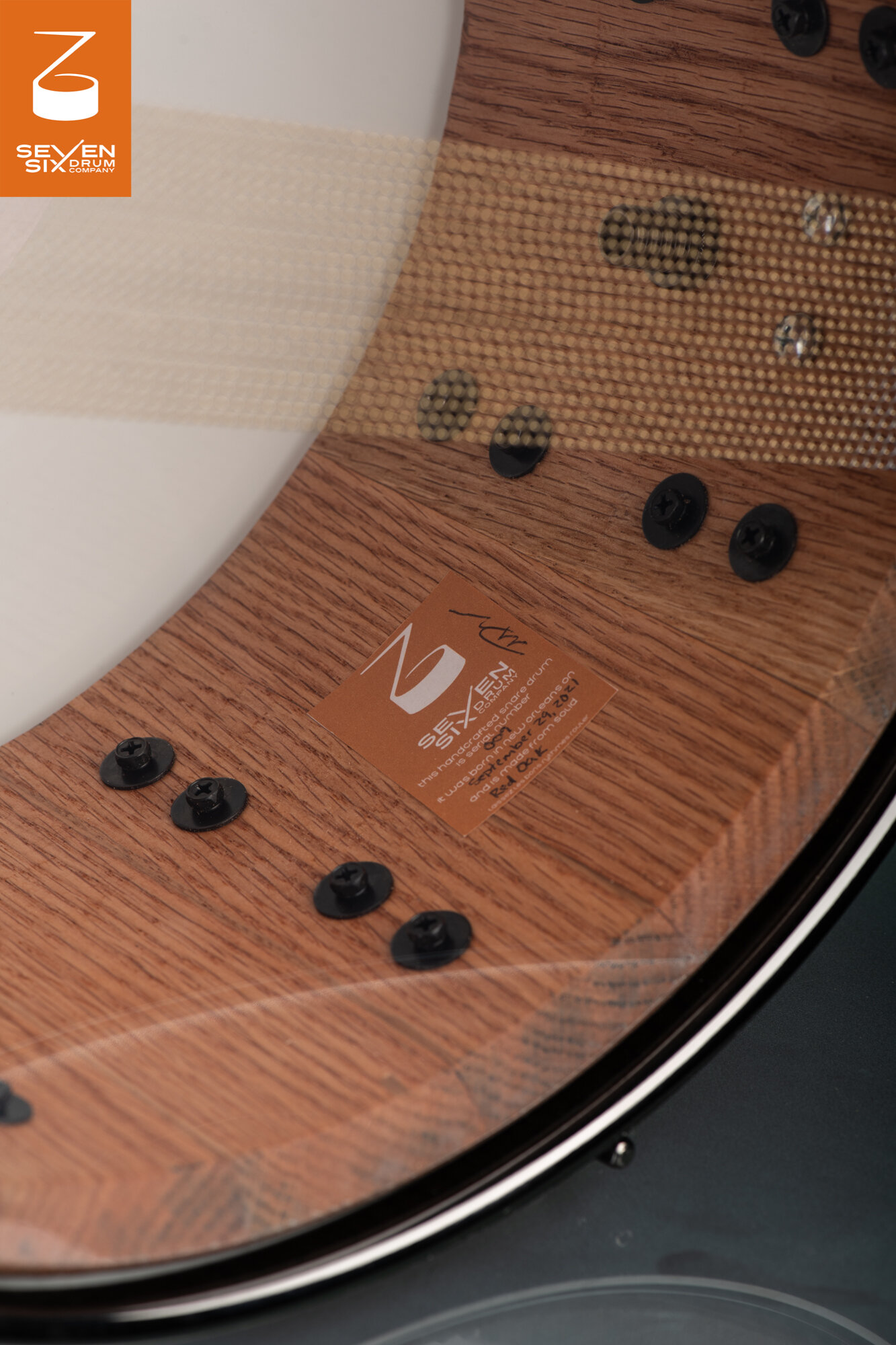 Interior of a solid red oak snare drum with a natural finish, maker's badge, and black mounting screws.