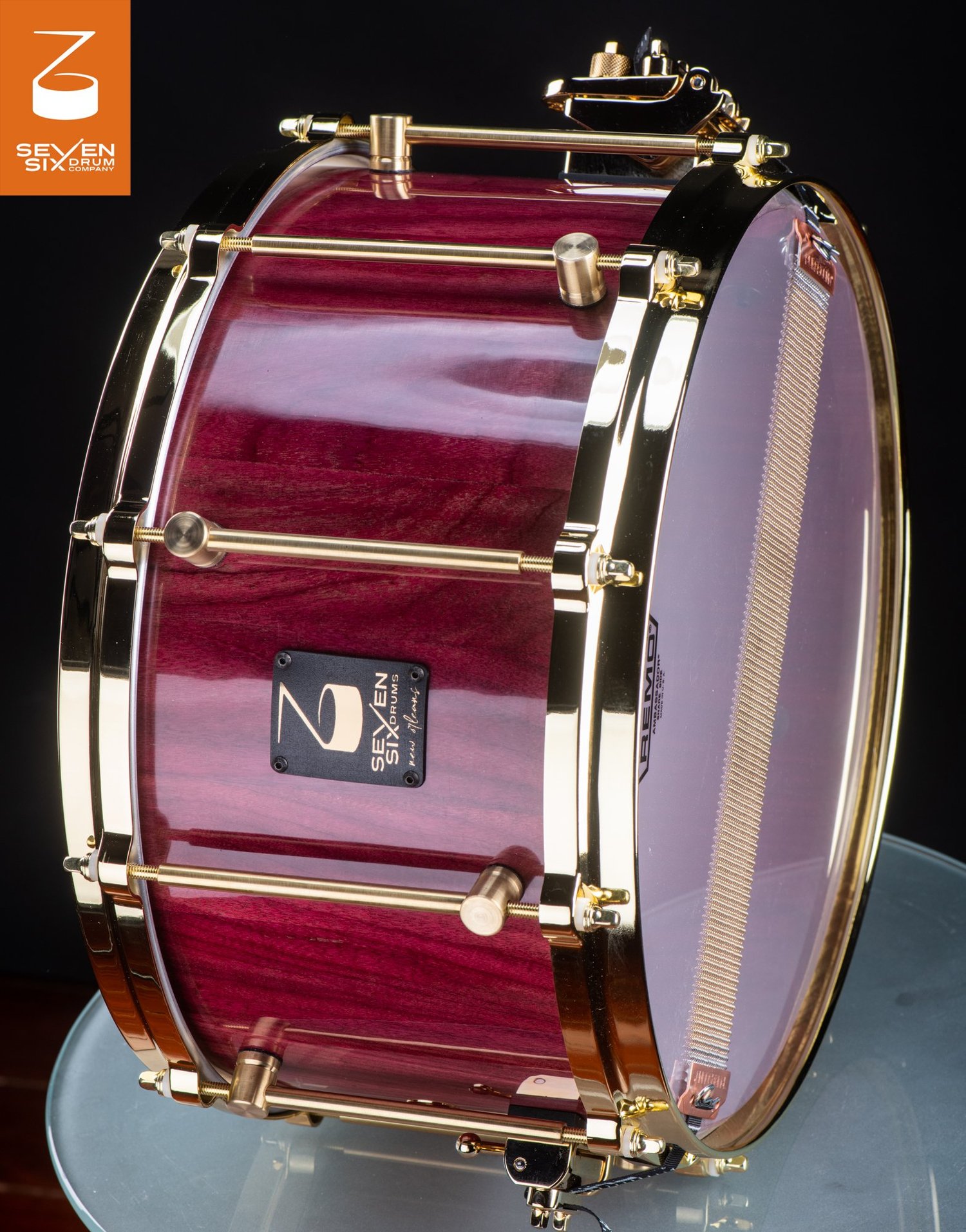 Deep snare drum with a glossy purpleheart wood shell, polished brass hoops, and tube lugs.