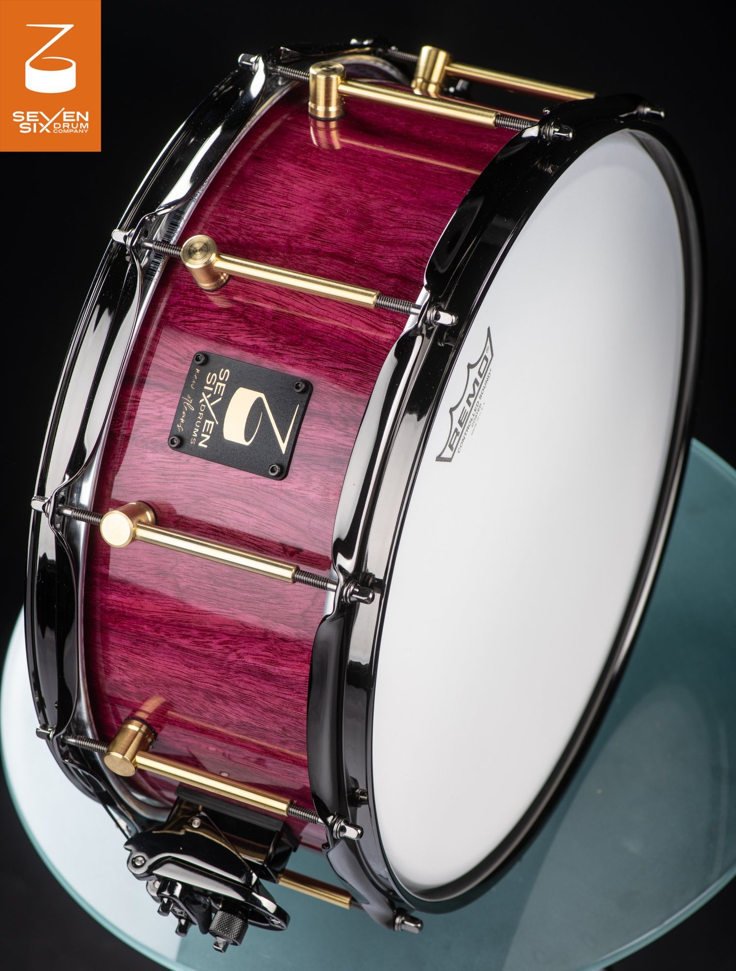 Handmade snare drum with a glossy purple wood shell, brass tube lugs, and black chrome hoops.