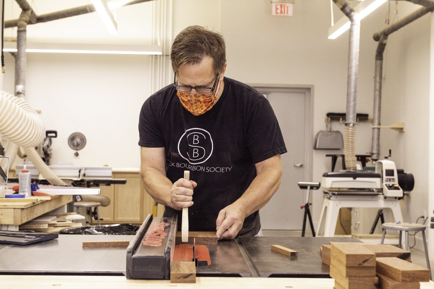 A craftsman cuts unfinished hardwood drum staves on a table saw using a wooden push stick.