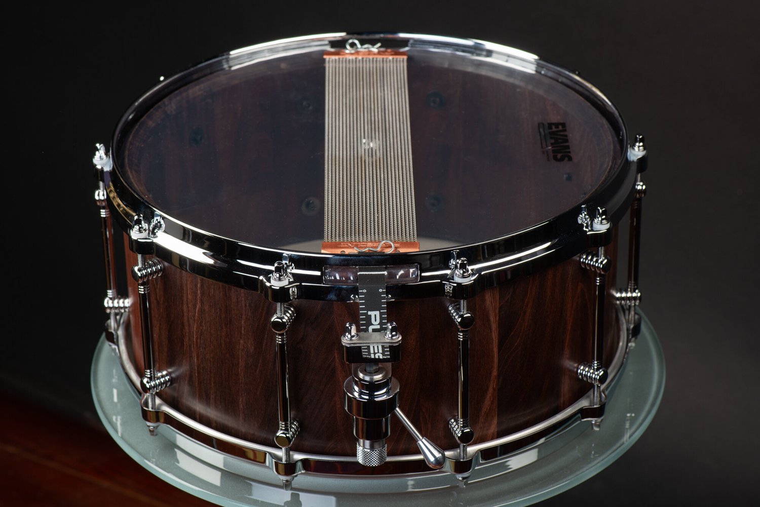 Handmade dark walnut snare drum with a satin finish, chrome tube lugs, and wire snares across a clear bottom head.