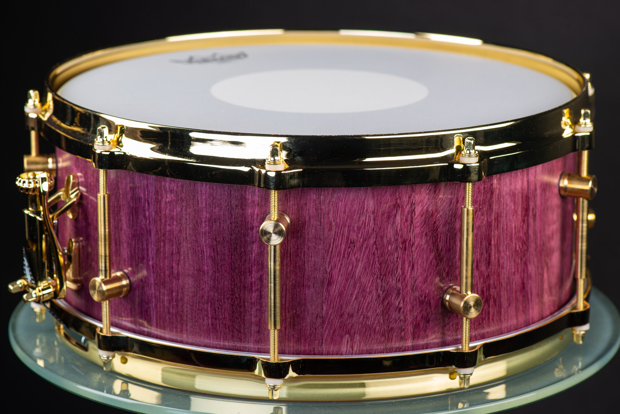 Handmade purpleheart wood snare drum with a satin finish, polished gold hoops, and brass tube lugs.