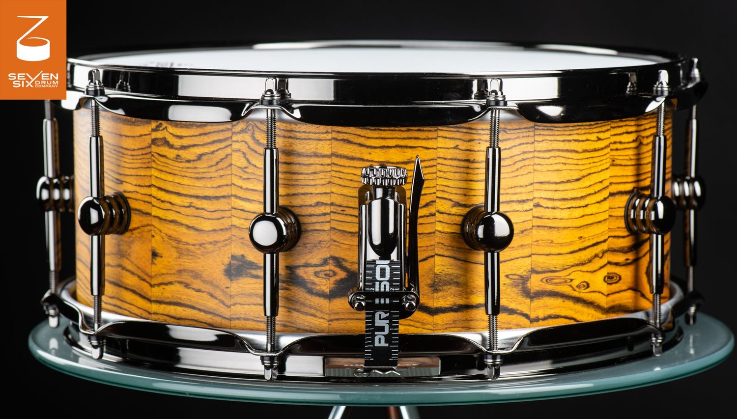 Handmade stave snare drum with a golden figured wood shell and polished black nickel hoops, lugs, and throw-off.