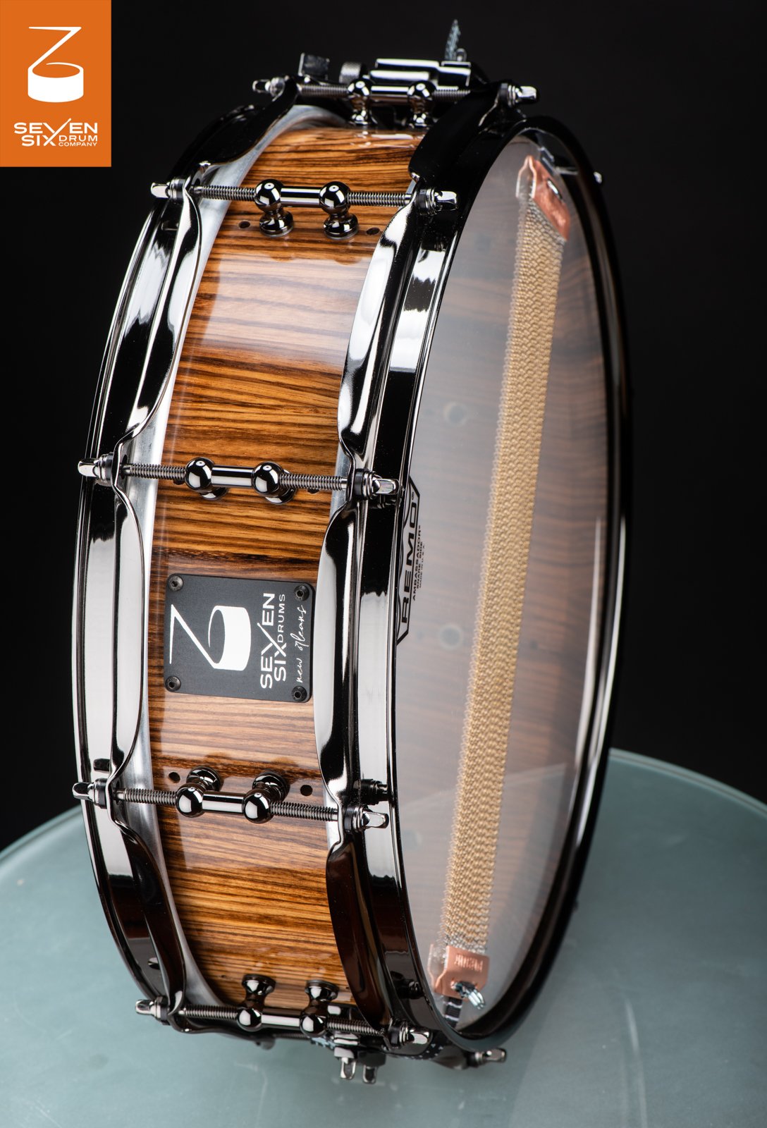 Handmade snare drum with a glossy zebrawood shell, polished black chrome hoops, and tube lugs.