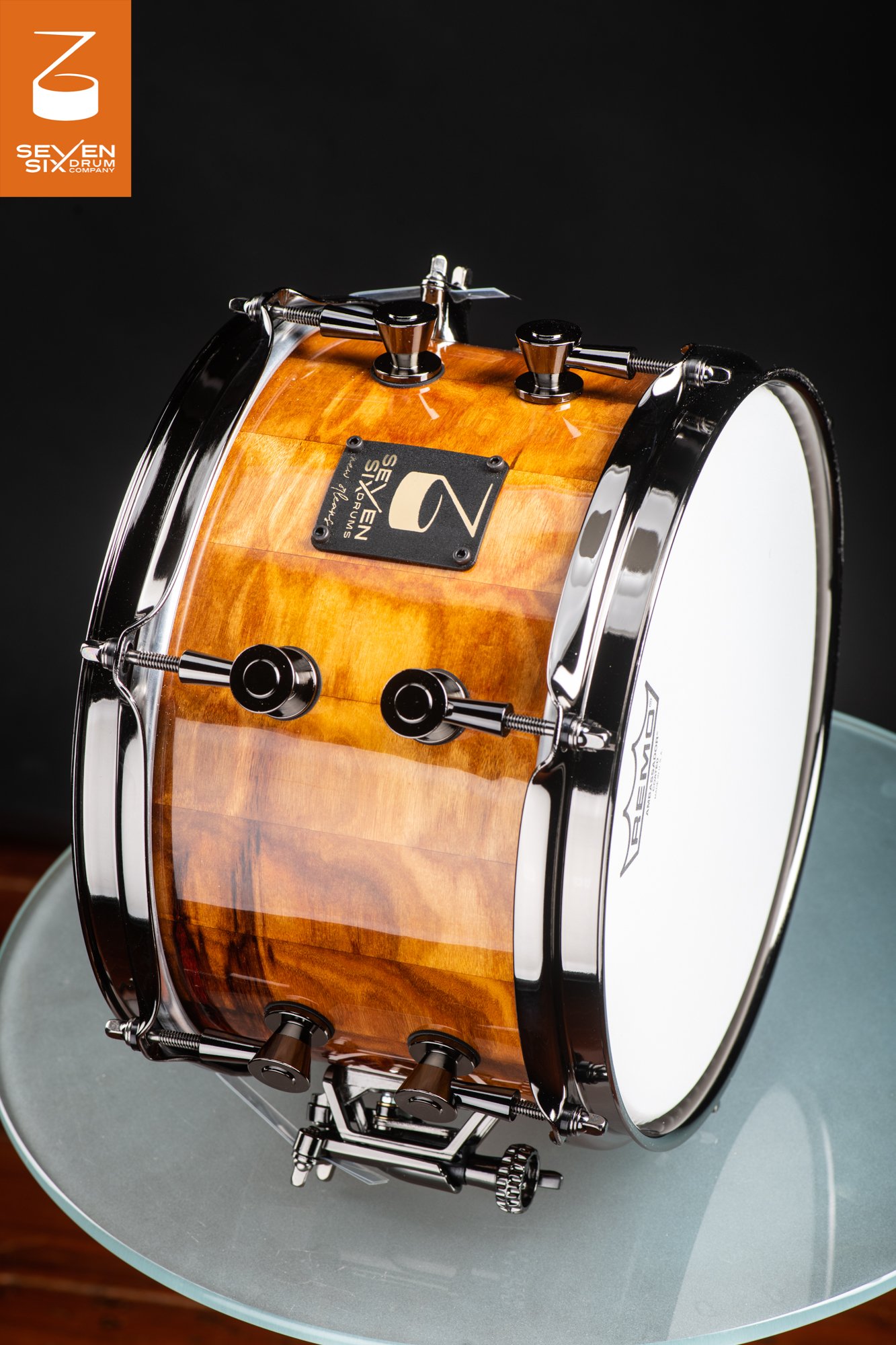 Handmade snare drum featuring a glossy natural wood shell with black nickel hoops and round lugs.