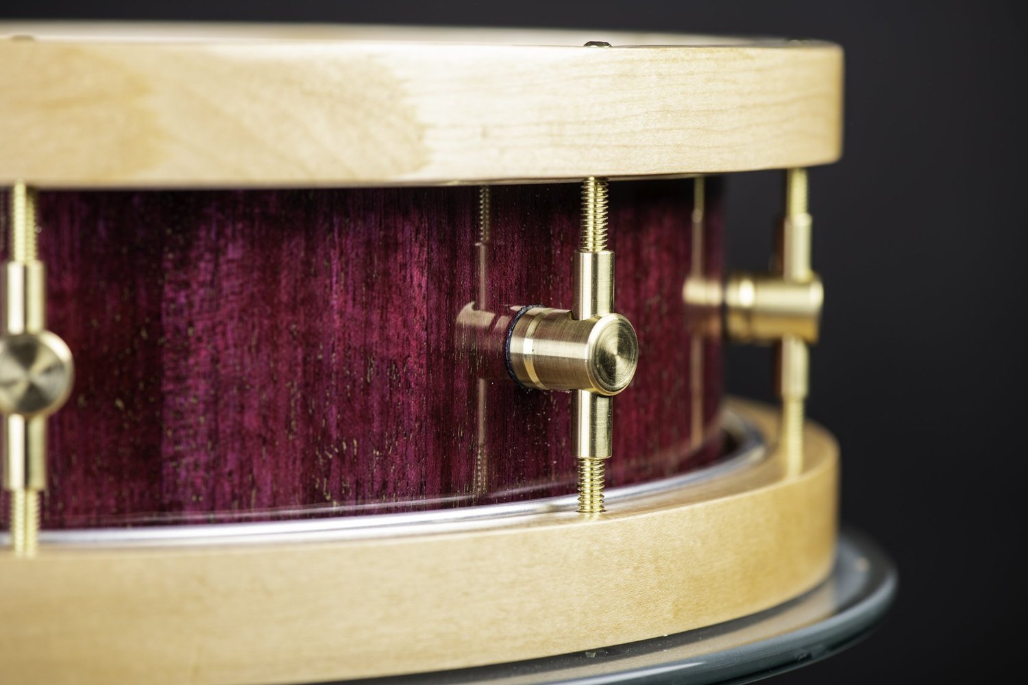 Handmade snare drum with a gloss purple wood shell, natural wood hoops, and machined brass lugs.