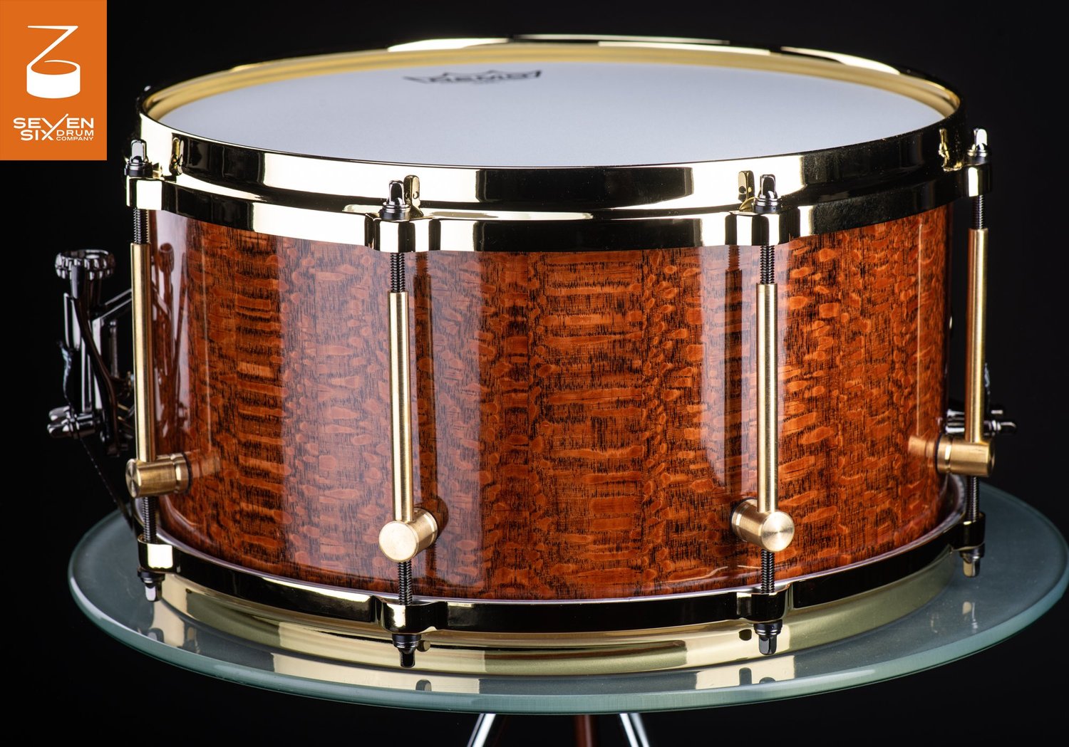 Handcrafted snare drum with a high-gloss figured wood shell, polished brass hoops, and tube lugs.