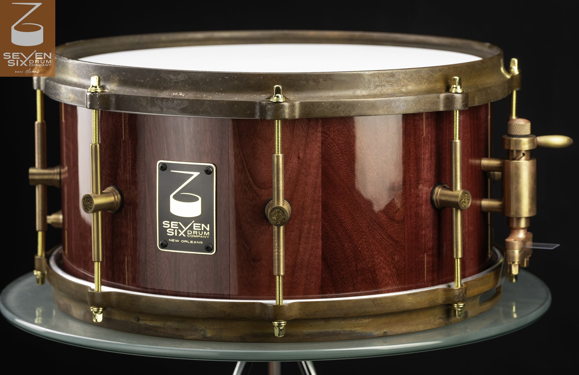 Handcrafted snare drum featuring a glossy red wood shell, antique bronze hoops, and matching brass hardware.