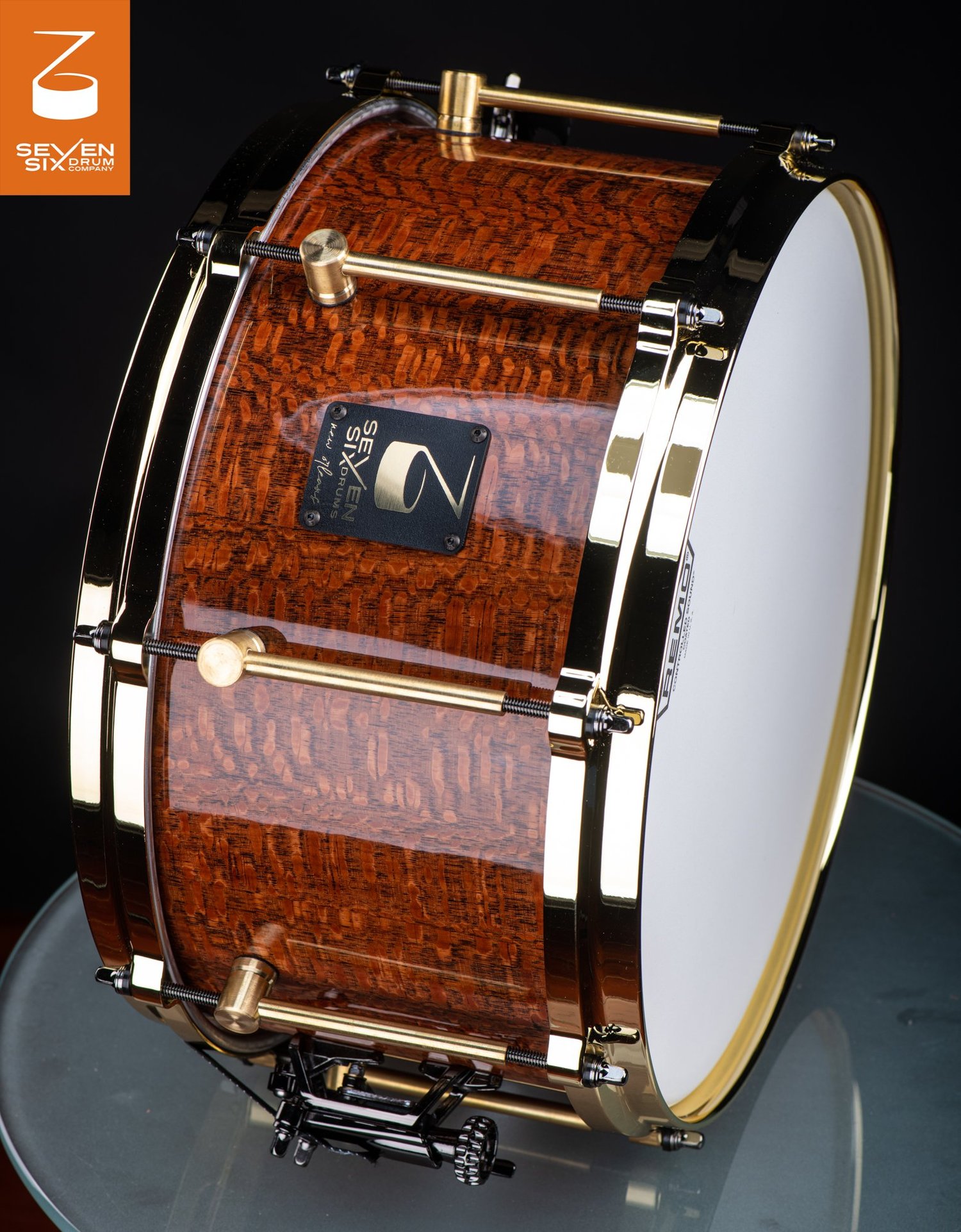 Snare drum with a glossy figured wood shell, polished brass hoops, and brass tube lugs.