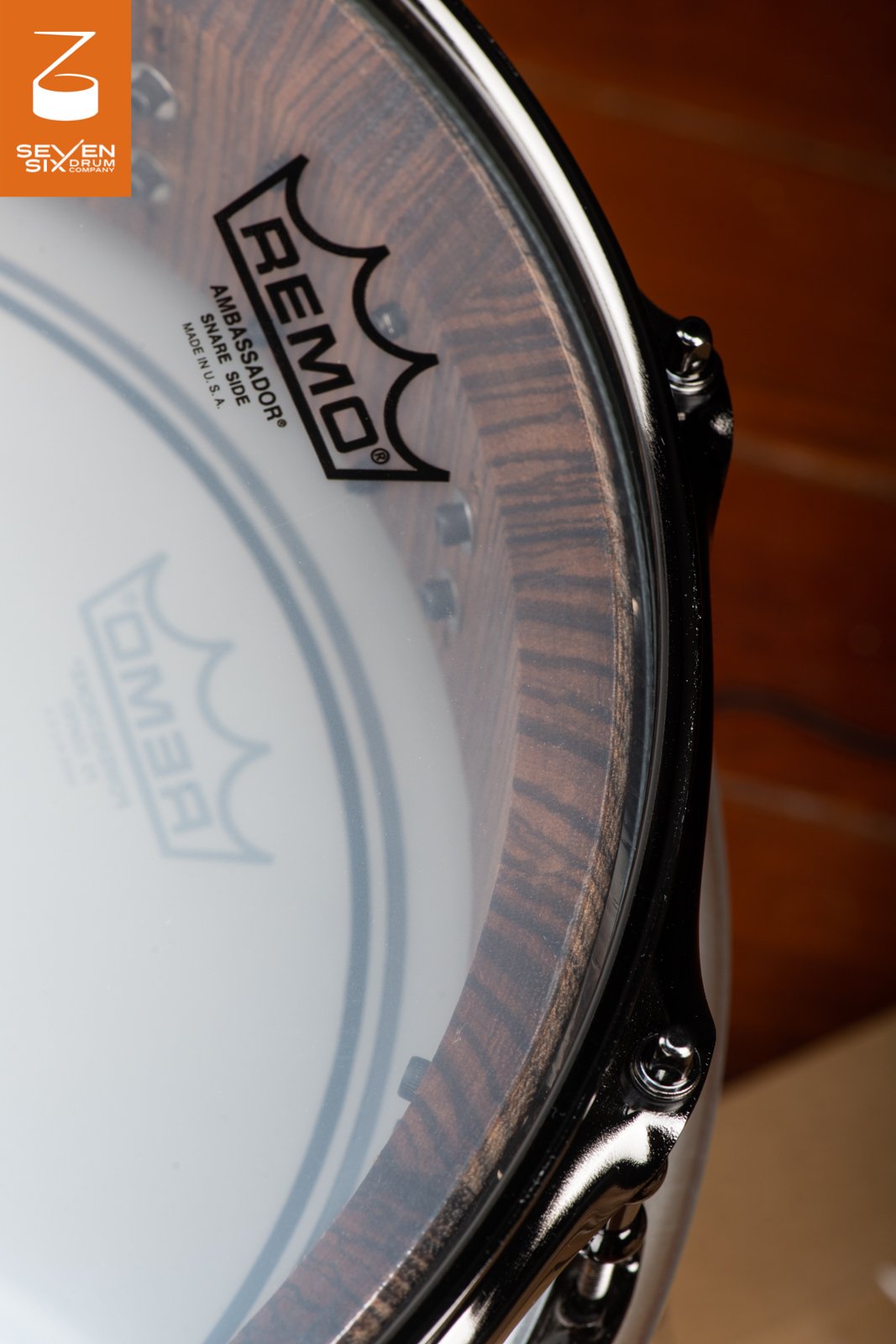 Snare drum interior with rich brown wood grain viewed through a clear Remo head bordered by a glossy black metal hoop.