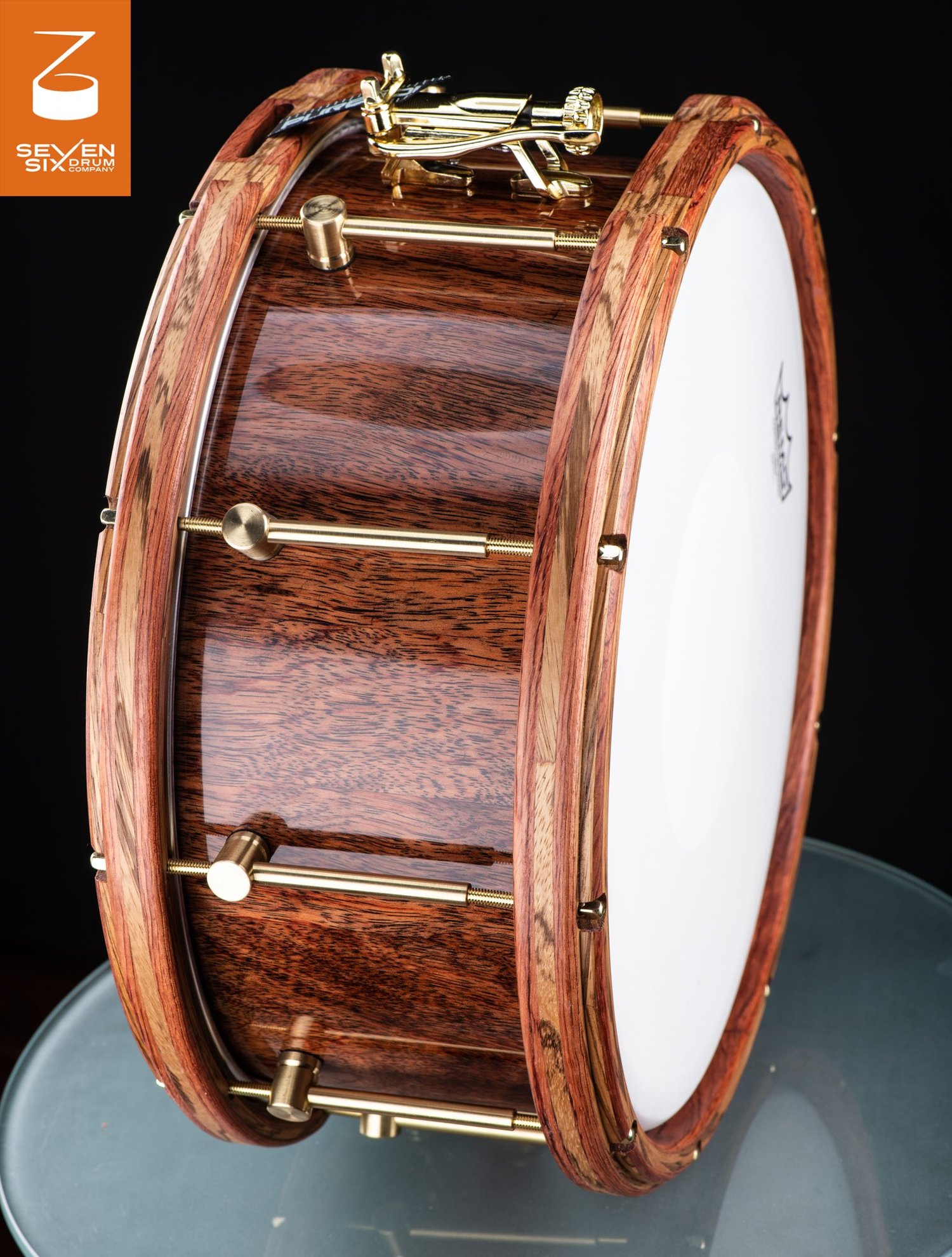 Handmade snare drum featuring a glossy wood shell, natural wood hoops, and polished brass tube lugs.