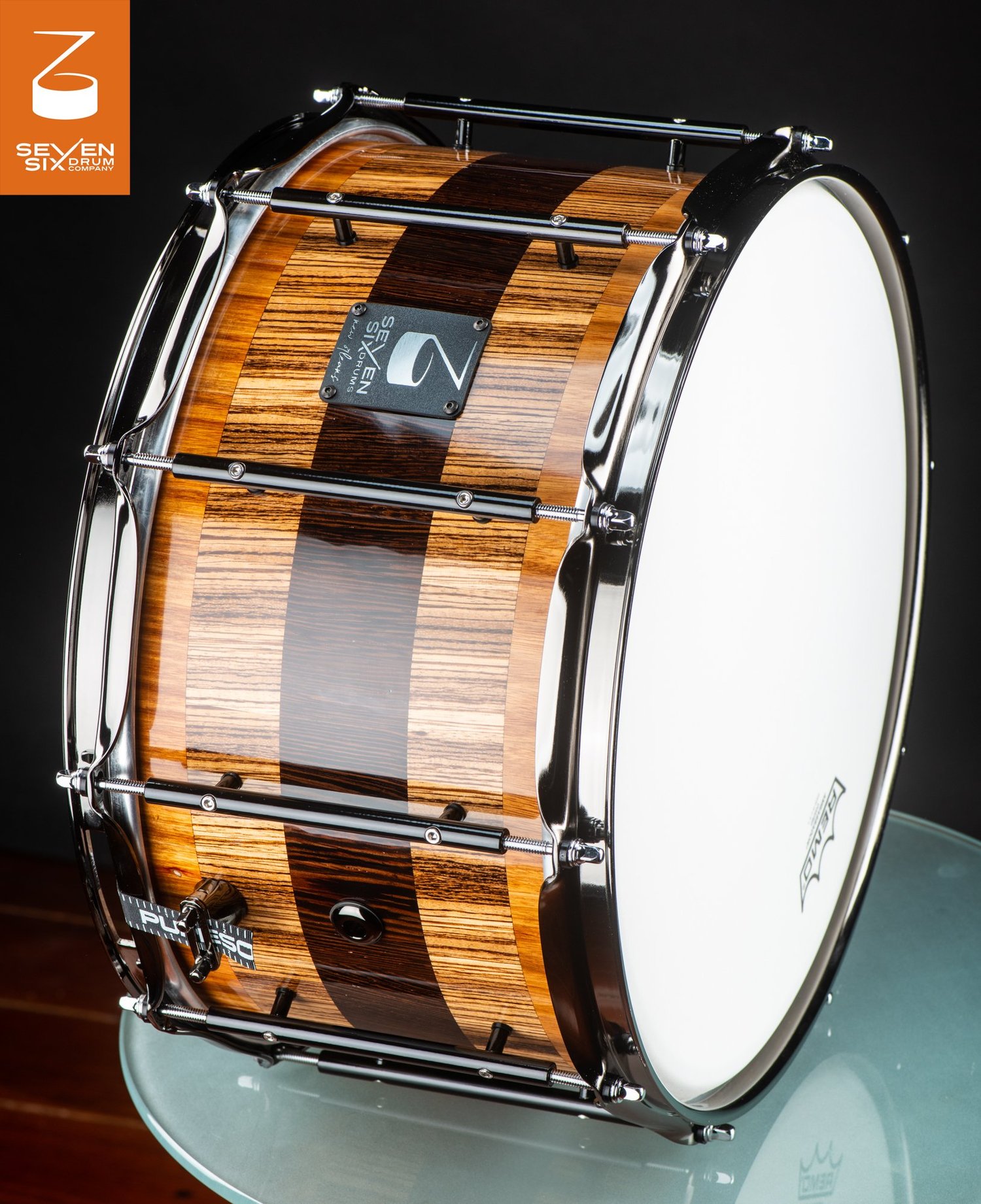 Handmade snare drum featuring a glossy striped wood shell with chrome hoops and black tube lugs.