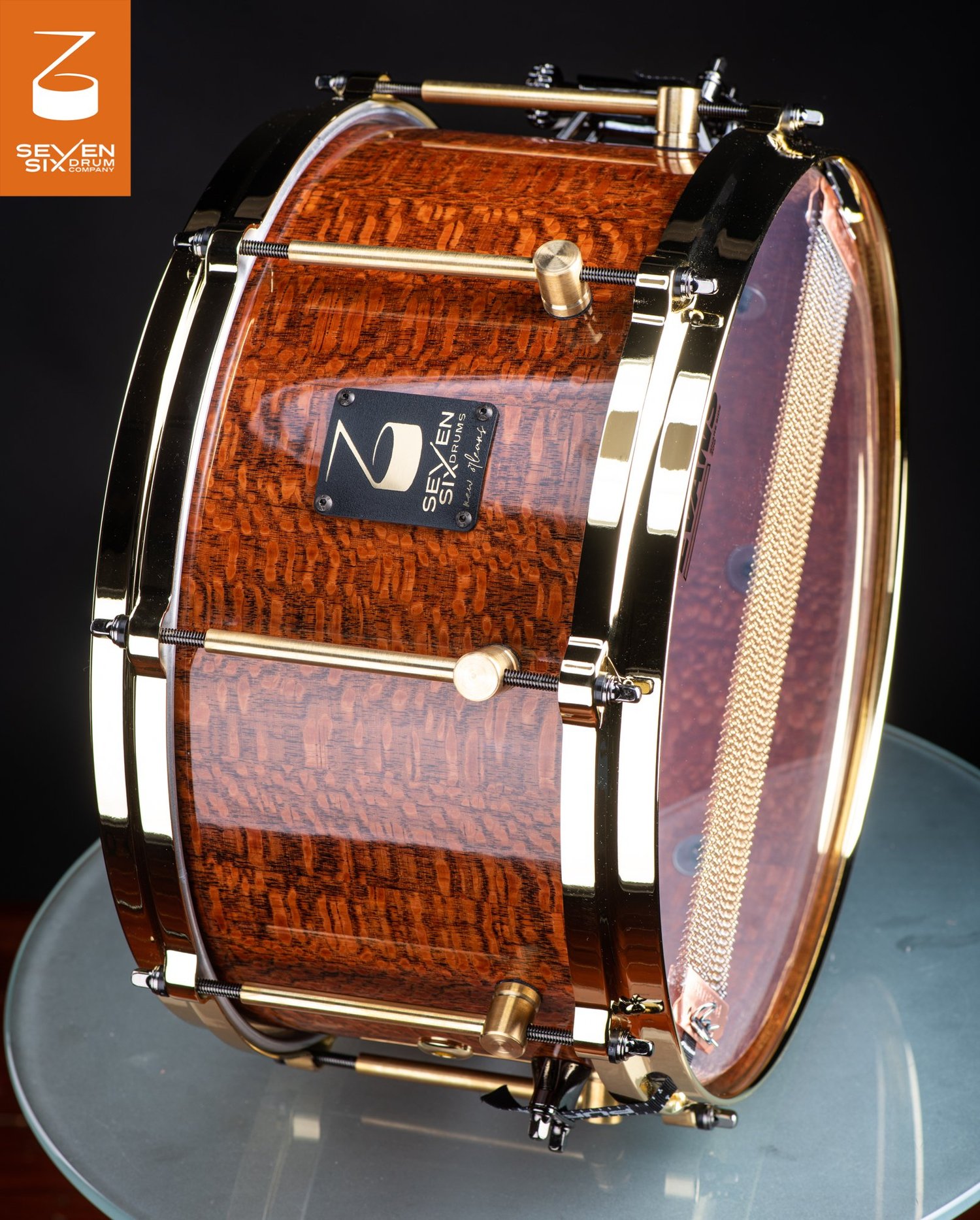 Handmade snare drum with a high-gloss figured wood shell, polished brass hoops, and brass tube lugs.
