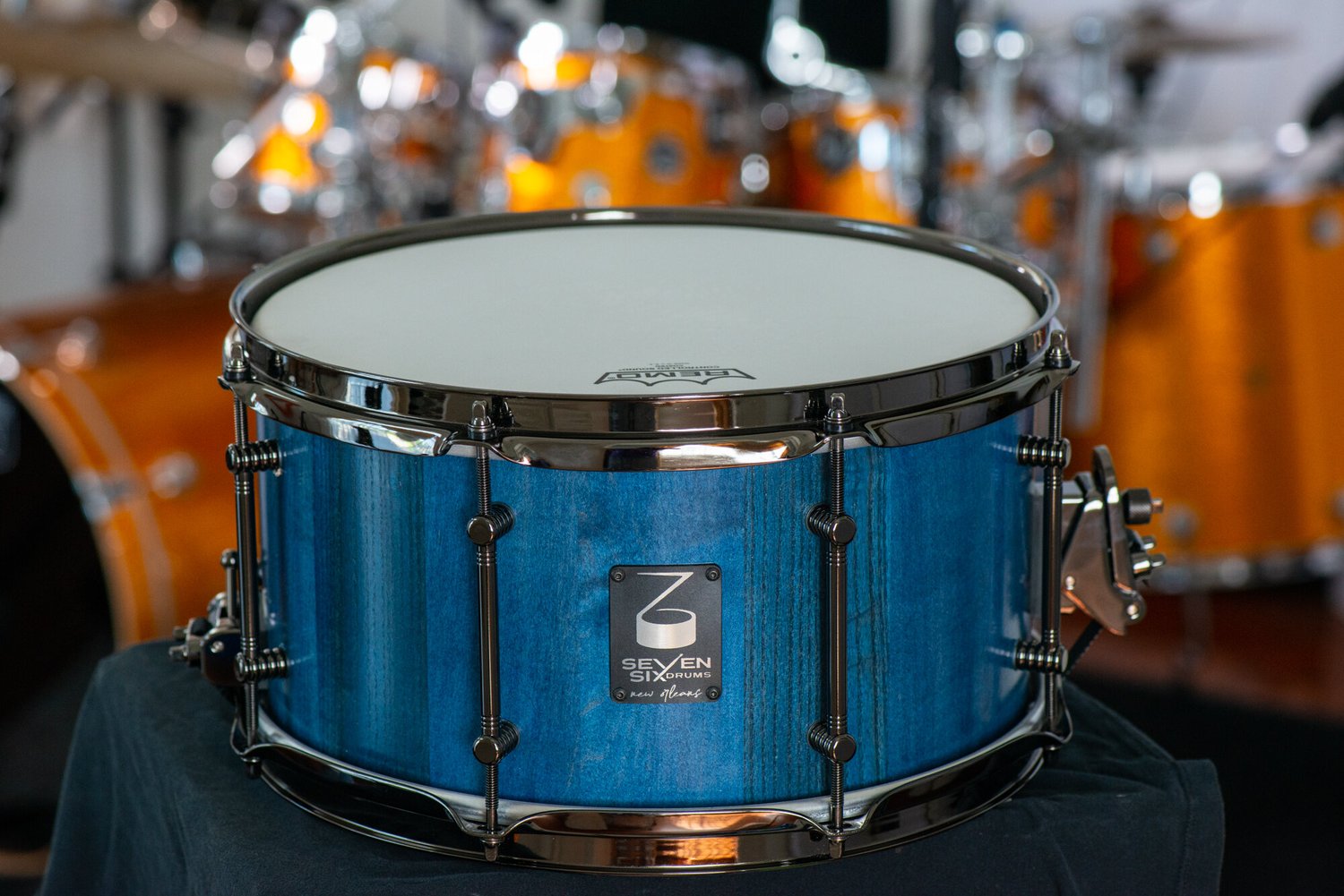 Blue stained wood snare drum featuring a visible grain finish with black nickel hoops and tube lugs.