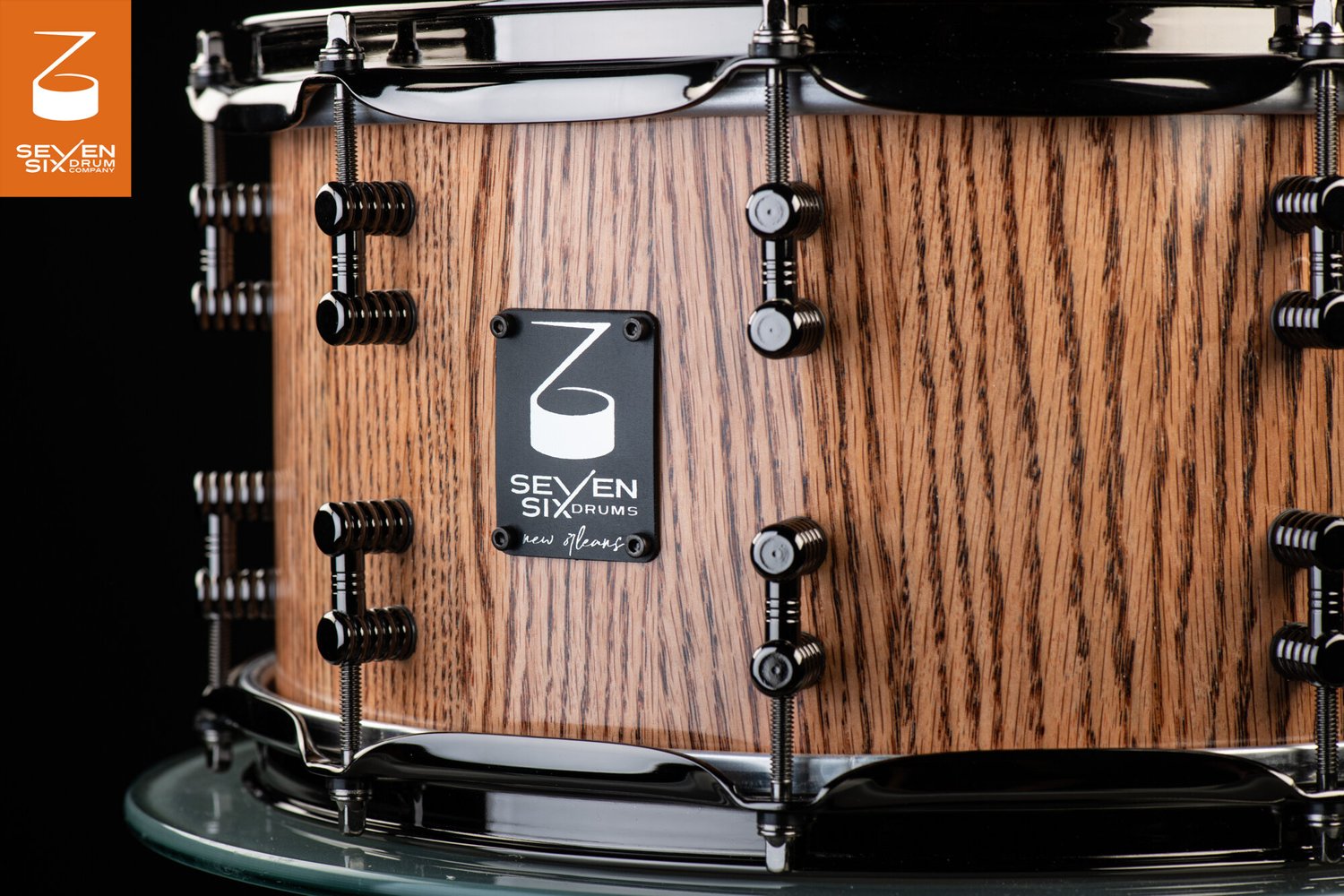 Handmade snare drum with a natural oak wood finish, glossy black hoops, and grooved black lugs.