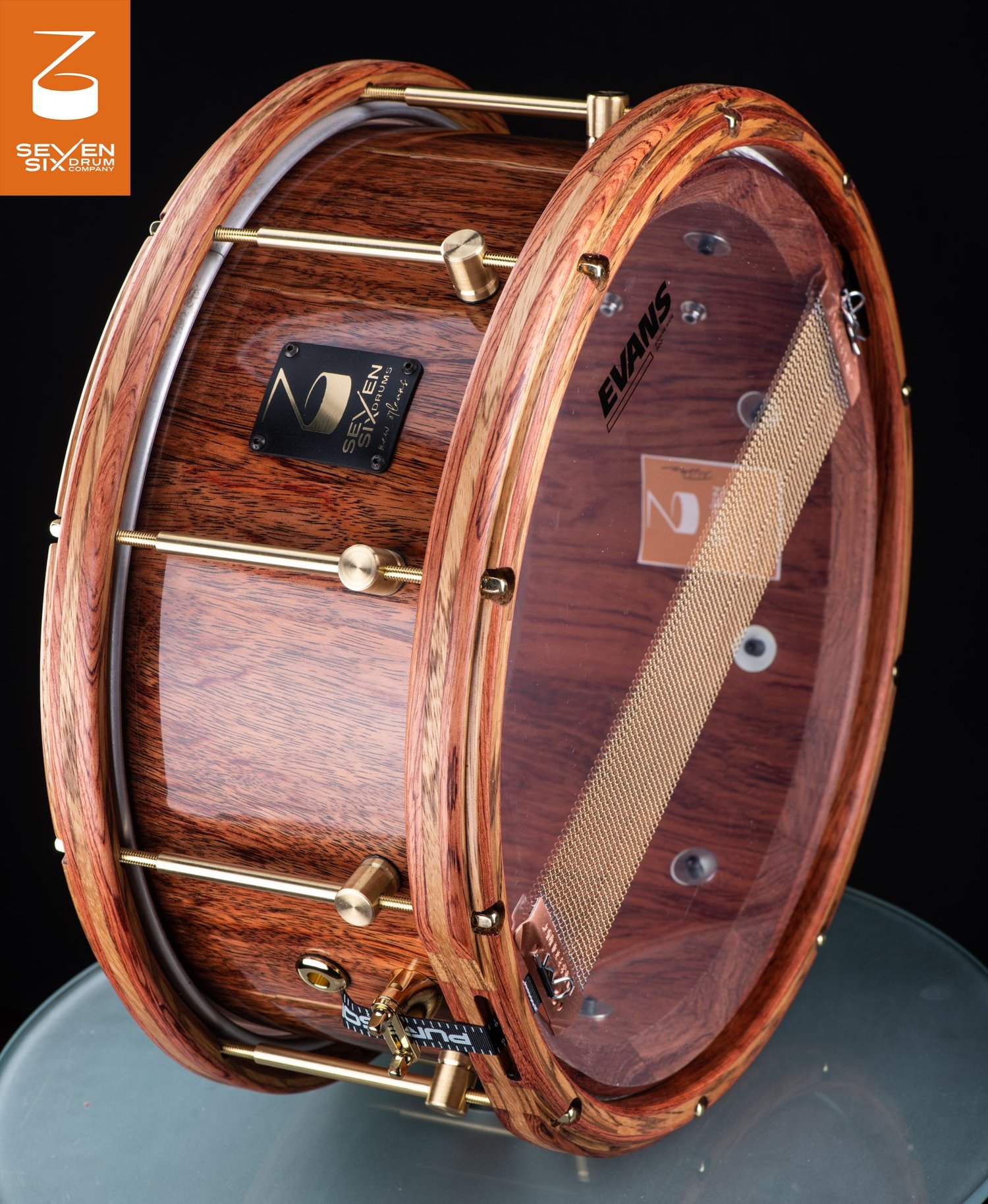 Gloss-finished wood snare drum featuring matching wooden hoops, brass tube lugs, and a clear resonant head.