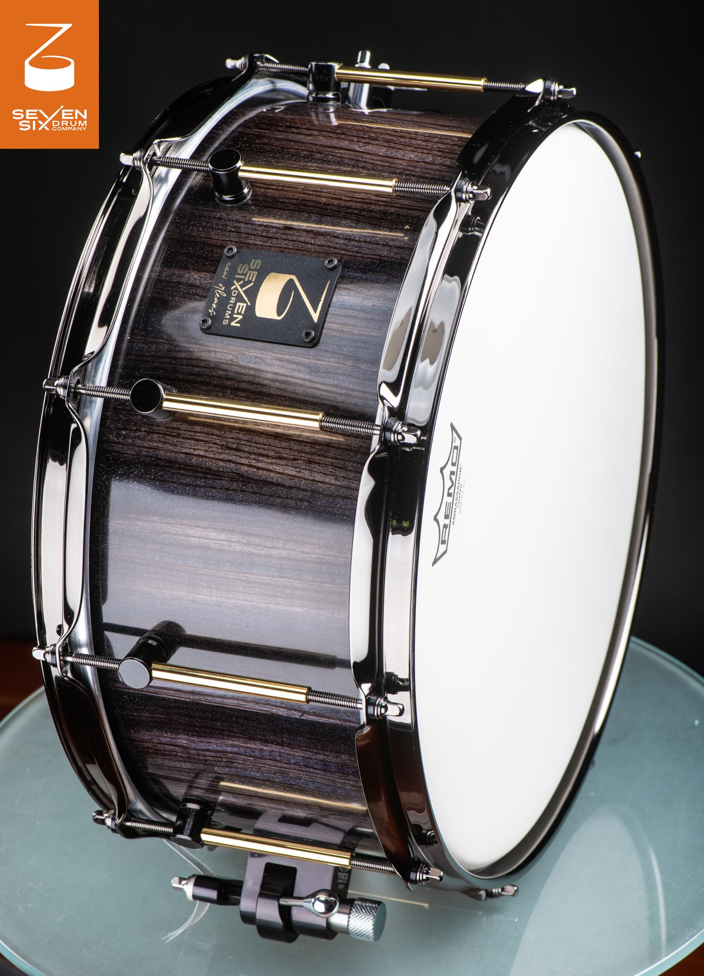 Handmade snare drum featuring a glossy dark wood shell, chrome hoops, and dual-tone brass and black tube lugs.