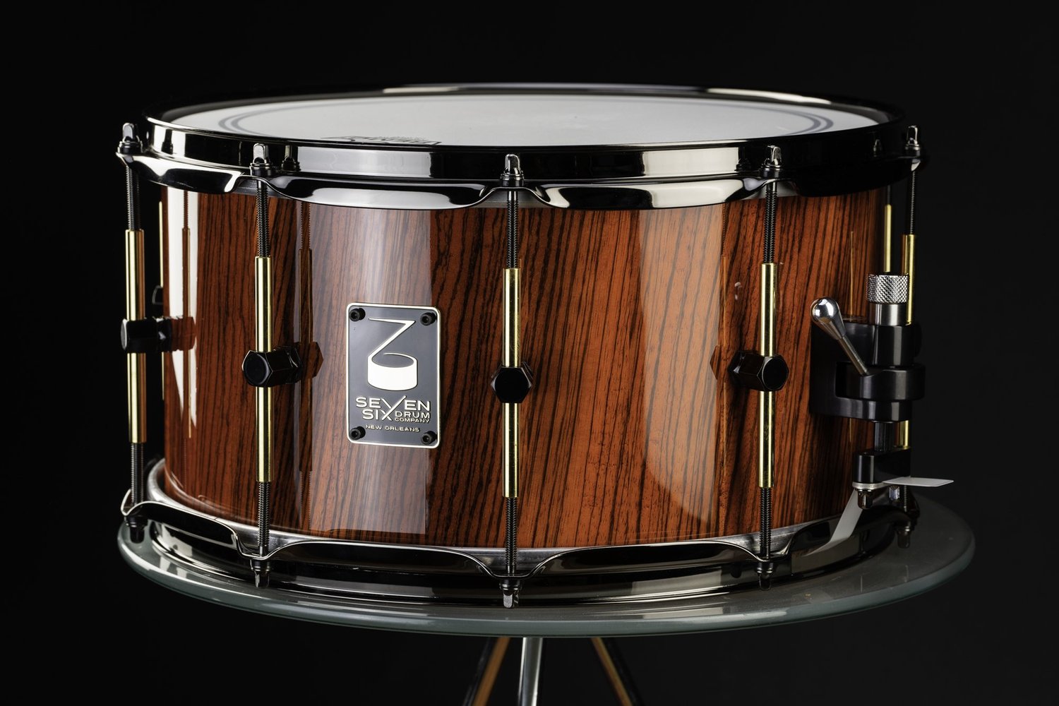 Handmade Zebrawood snare drum with a glossy reddish-brown wood shell, dark chrome hoops, and brass tube lugs.