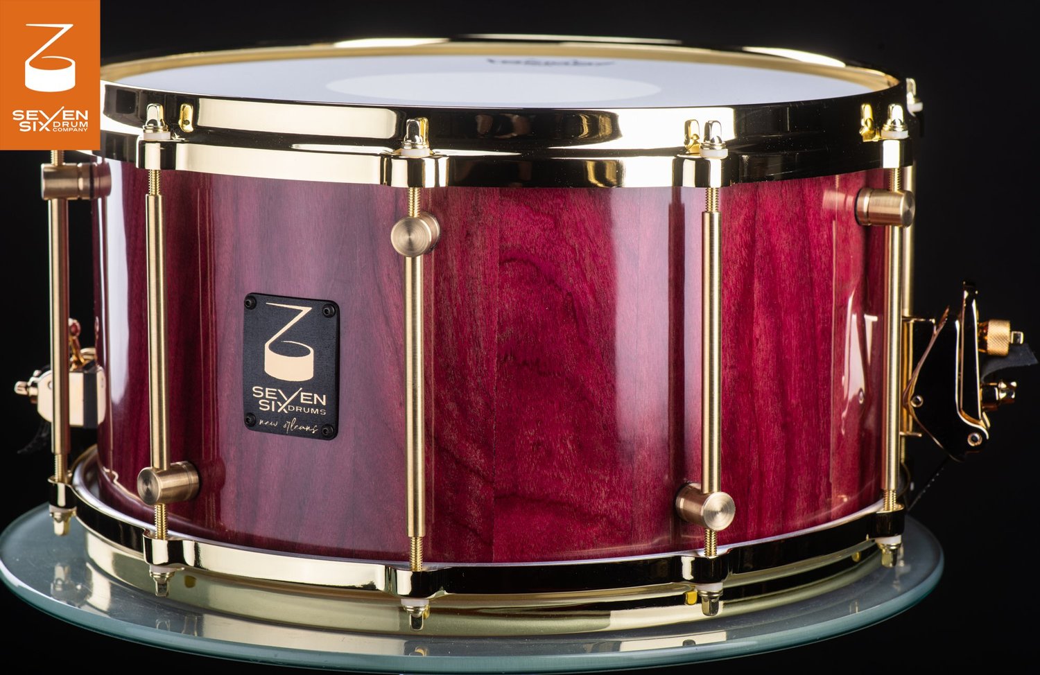 Handmade snare drum with a glossy purpleheart wood shell, polished brass hoops, and brass tube lugs.