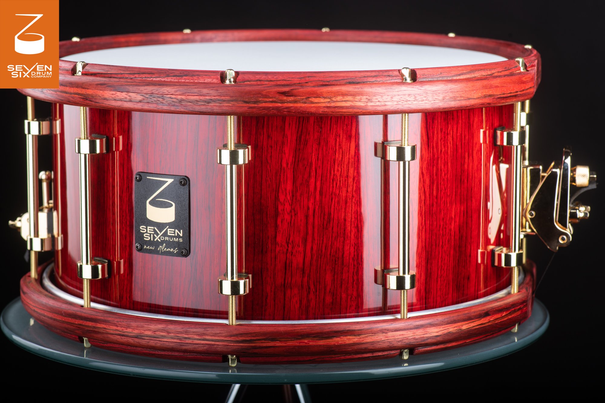 Glossy red wood snare drum featuring matching wooden hoops and polished brass tube lugs.