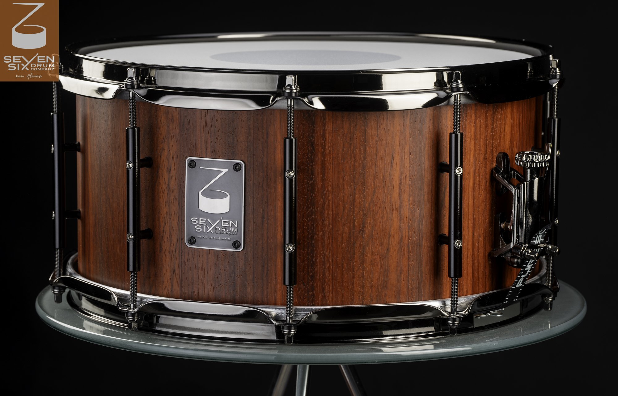 Handmade snare drum with a reddish satin wood shell, black tube lugs, and dark chrome hardware.