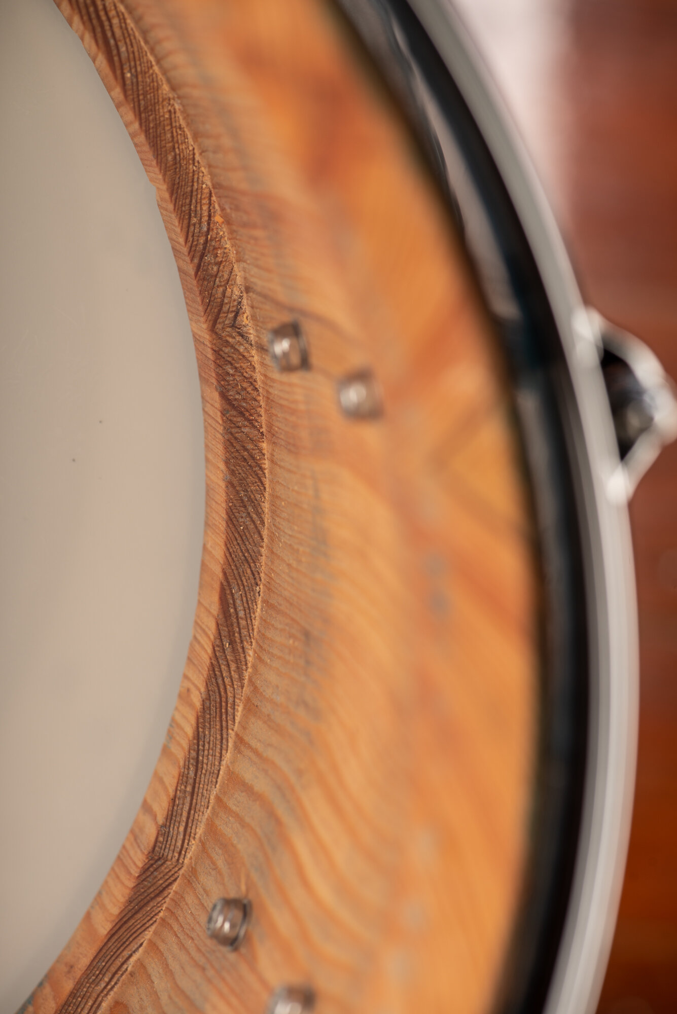 Interior of a snare drum shell showing natural-finish wood grain, chrome mounting screws, and an outer metal hoop.