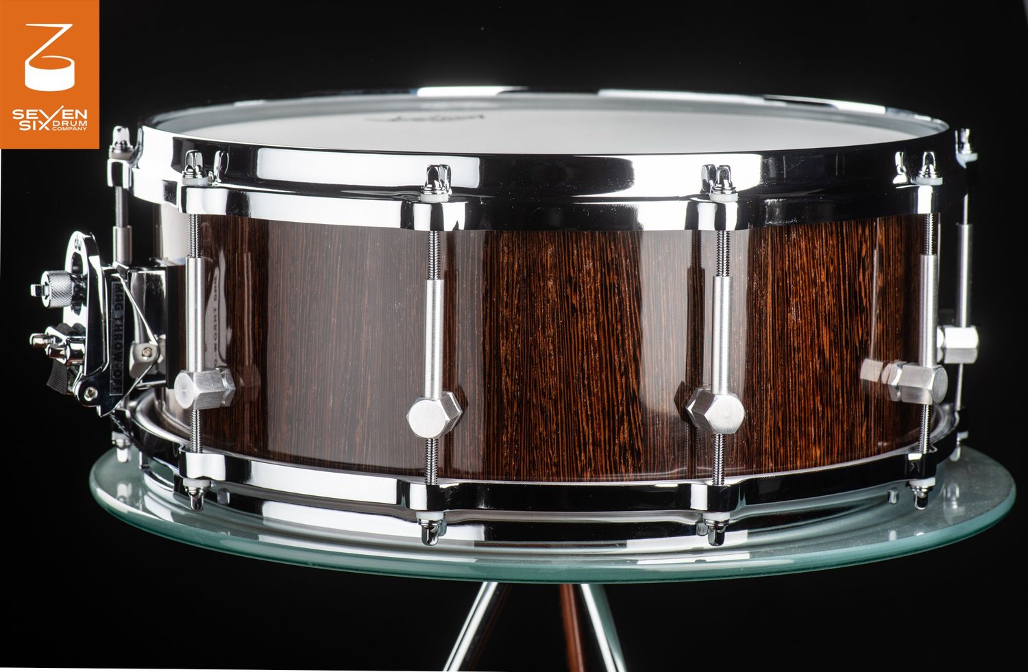 Handmade snare drum featuring a high-gloss dark wood shell with chrome hoops, hex lugs, and a MAG throw-off.