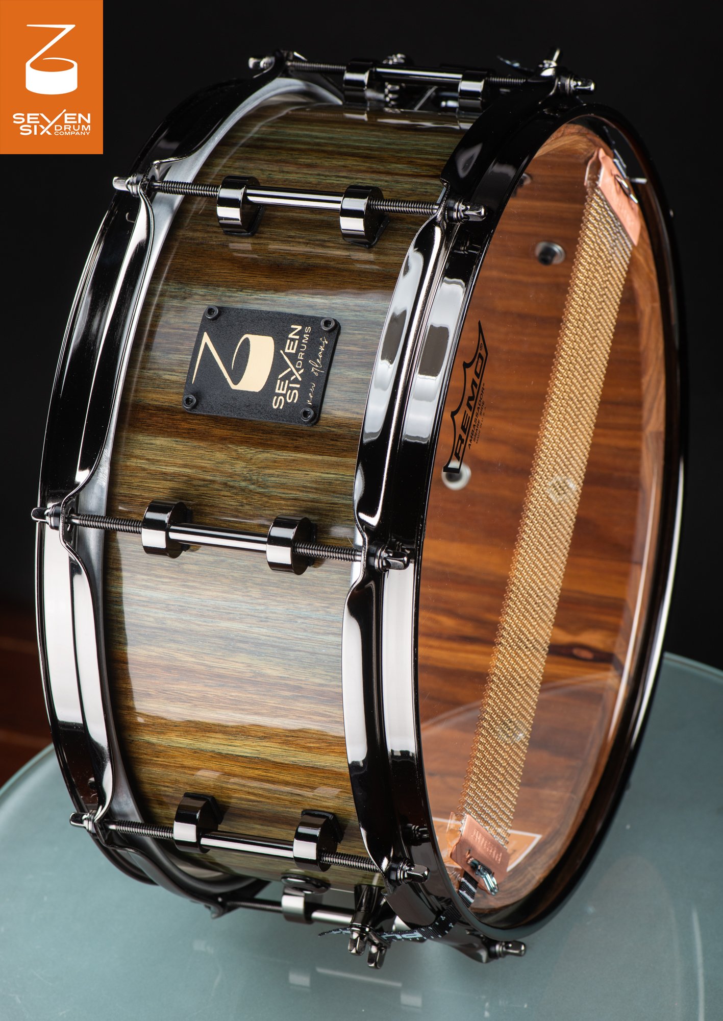 Handmade snare drum featuring a glossy green-tinted wood shell, black nickel hardware, and wide bronze snare wires.