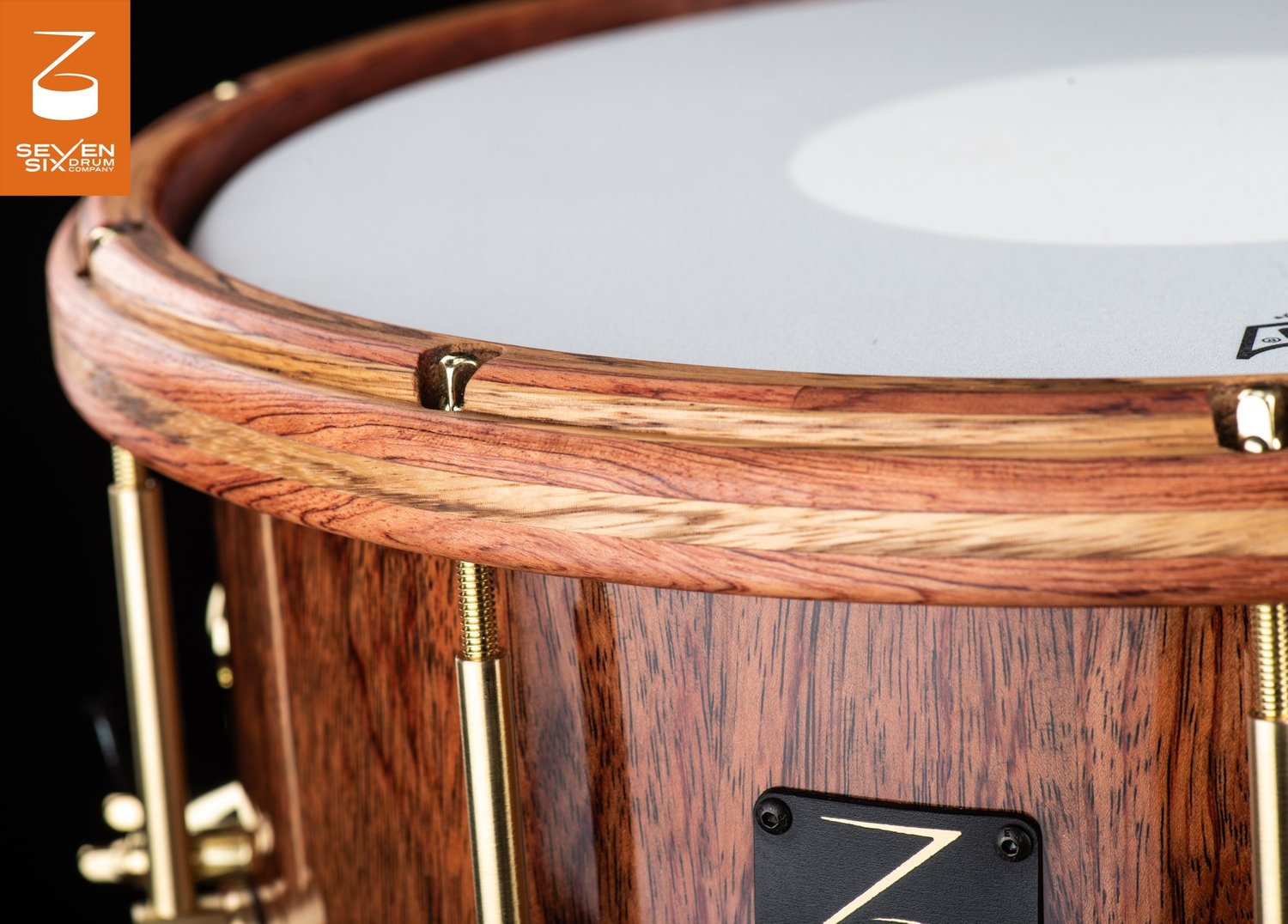 A glossy wood snare drum featuring a matching laminated wooden hoop and brass tension rods.