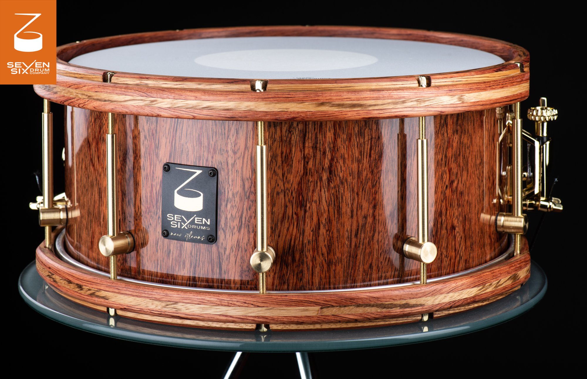 Handmade snare drum featuring a glossy wood shell, matching wooden hoops, and brushed brass tube lugs.
